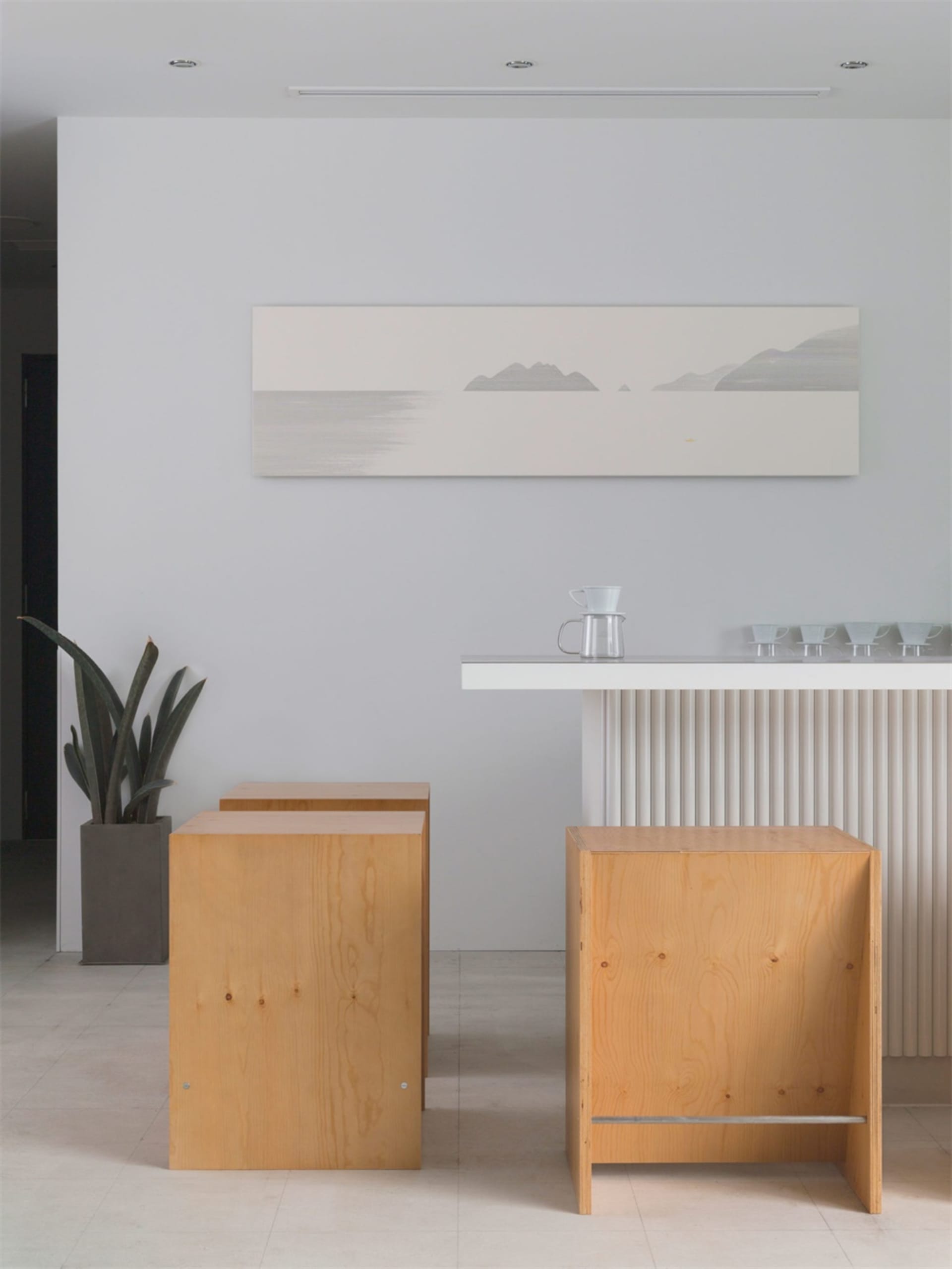 Minimalist design featuring wooden stools, a white counter, and a serene seascape painting.