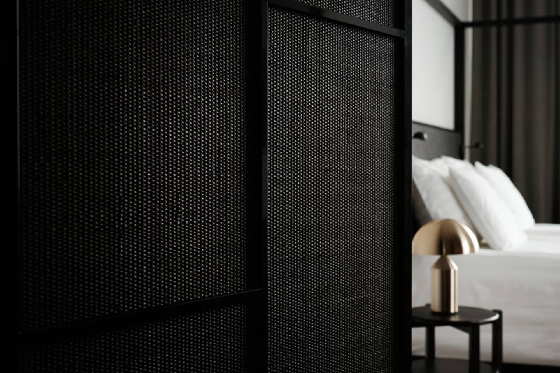 Close-up of a minimalist bedroom featuring a textured wall panel and a modern bedside lamp on a nightstand.