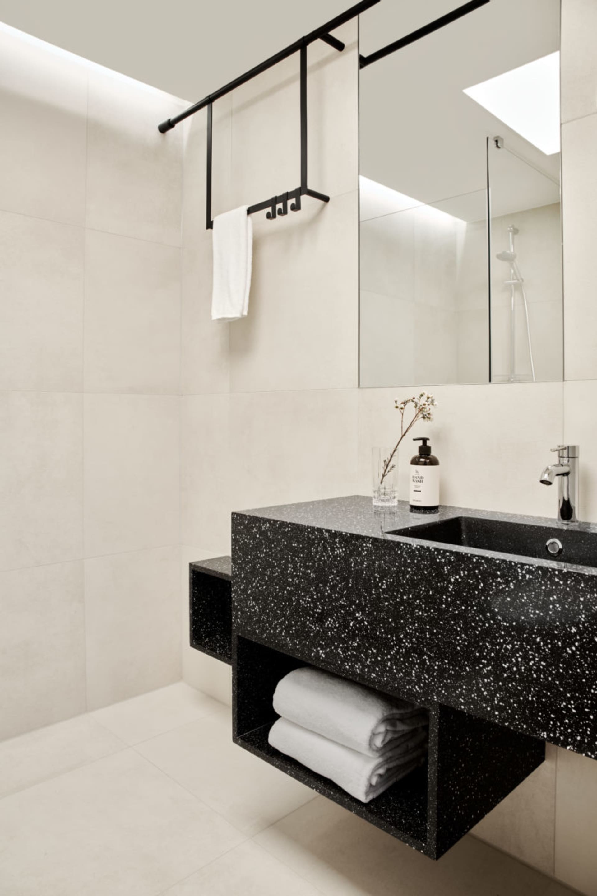 A modern black concrete bathroom with a floating vanity, white towels, and a glass mirror.