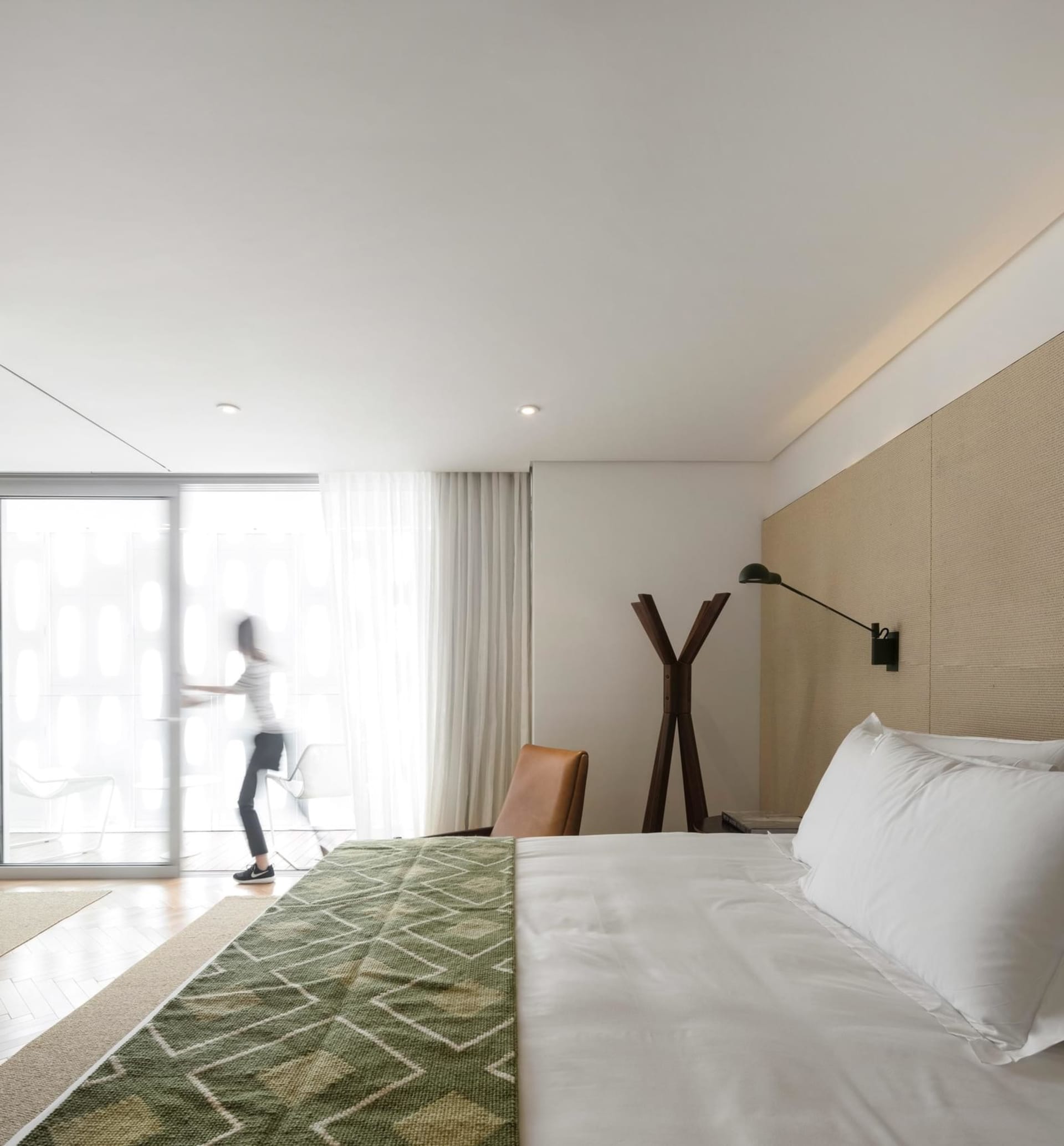 Minimalist bedroom with a textured wall, featuring a bed with white bedding and a green throw rug, and a sleek, modern design