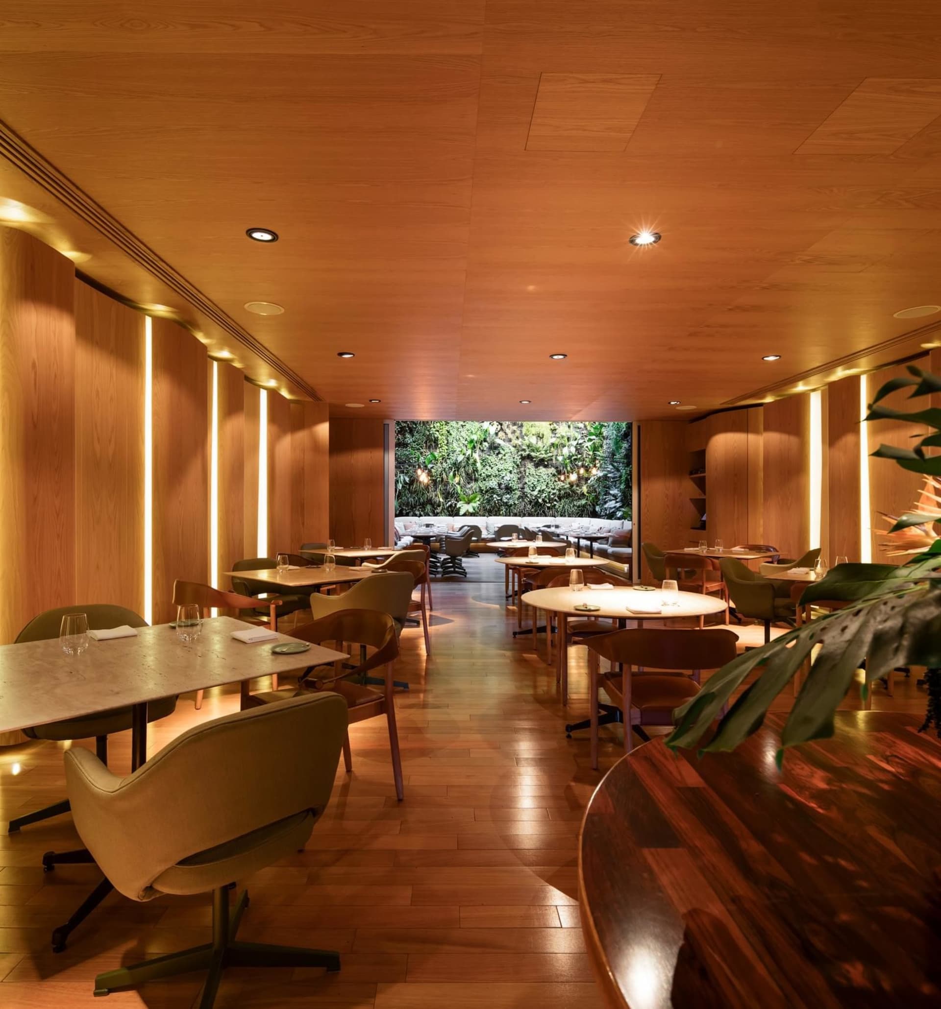 A modern restaurant interior designed with wooden tables, chairs, and walls, complemented by glass elements and industrial li