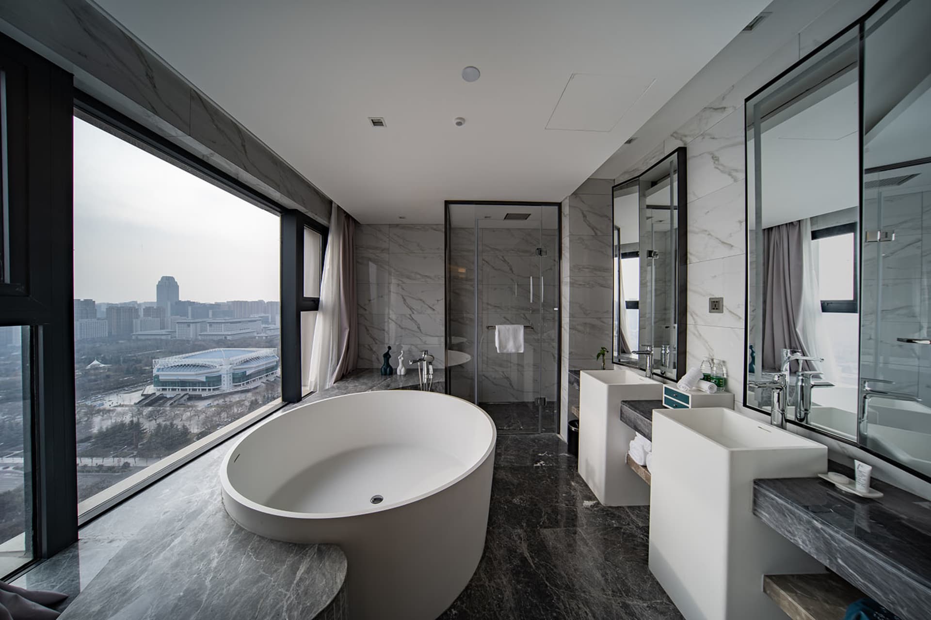 Modern bathroom featuring a freestanding bathtub with a cityscape view through large windows and marble flooring.