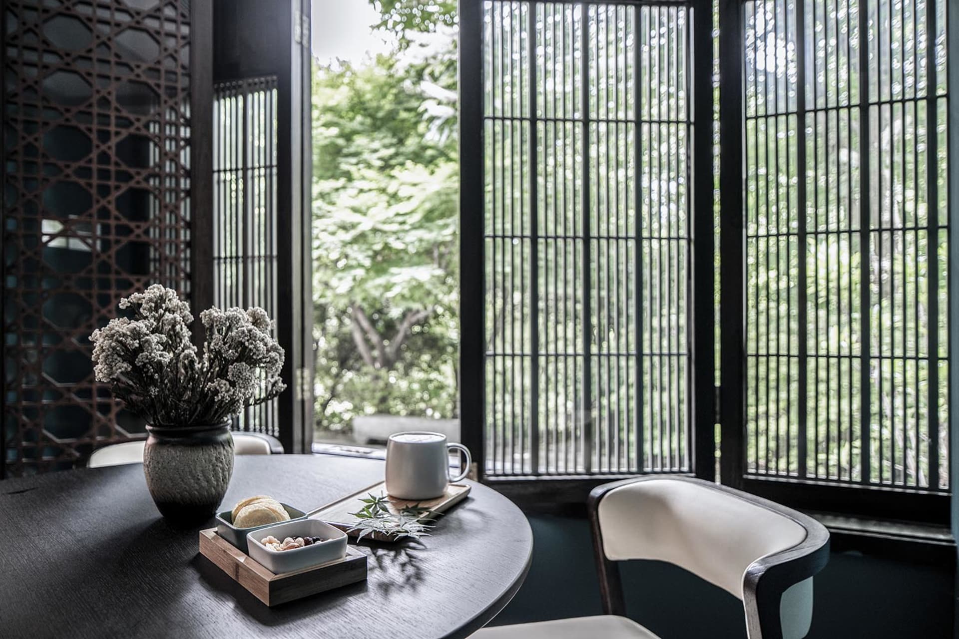 A cozy coffee shop with a wooden table, white chairs, and a vase of flowers.