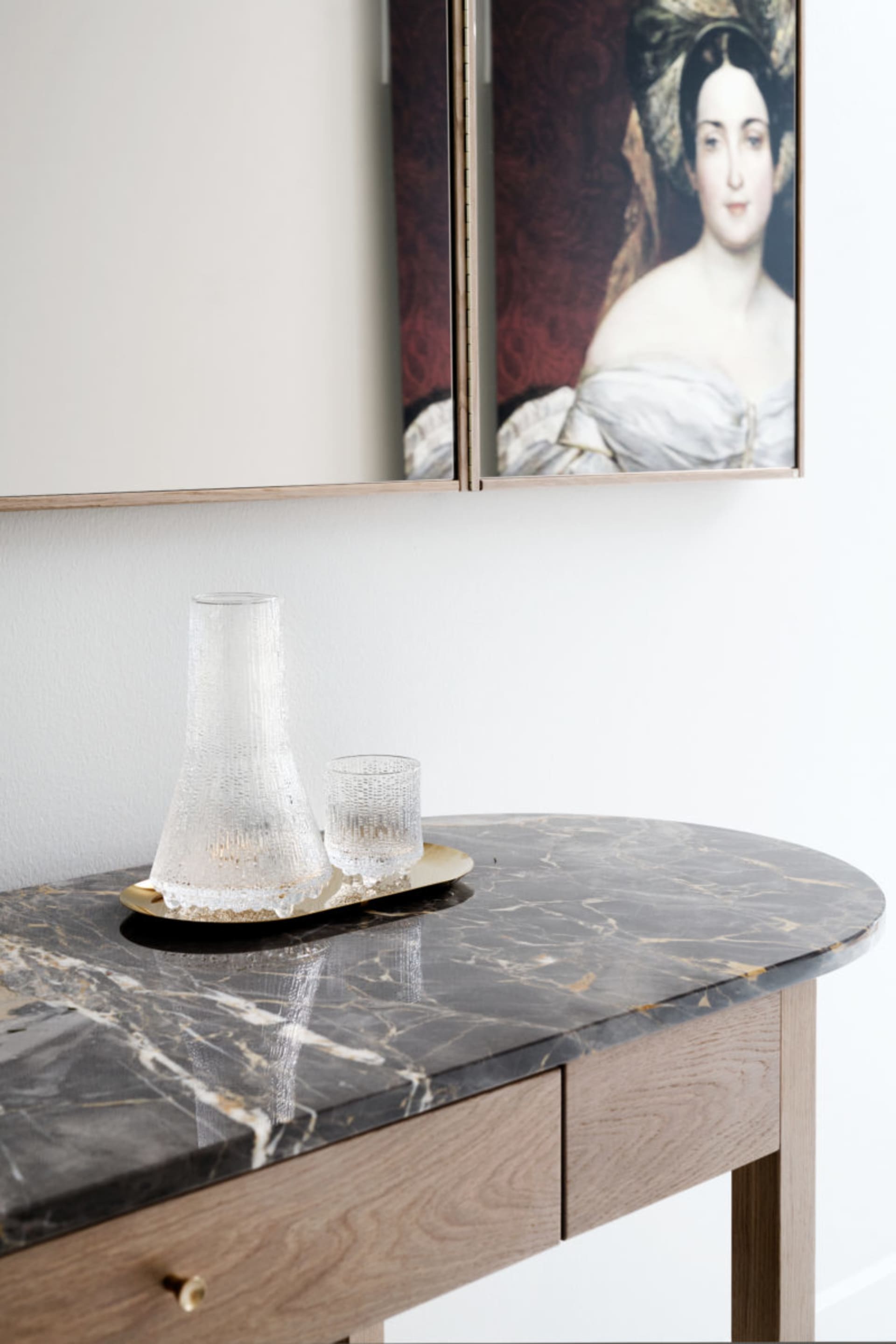 A modern vanity table with a black marble top features a glass vase and a matching glass tumbler.