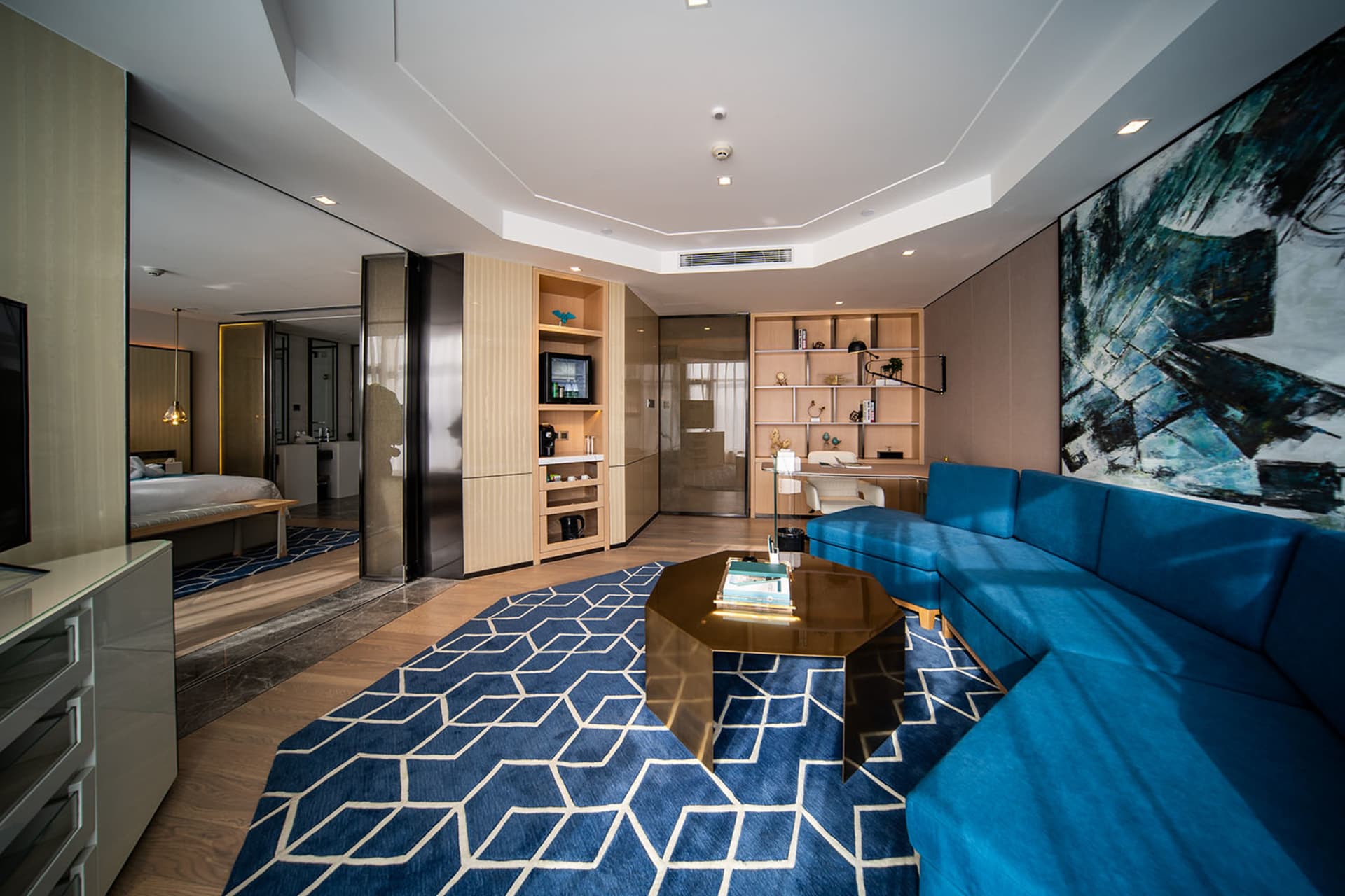 Modern living room featuring a blue sectional sofa, wooden coffee table, and glass panel divider with stainless steel accents