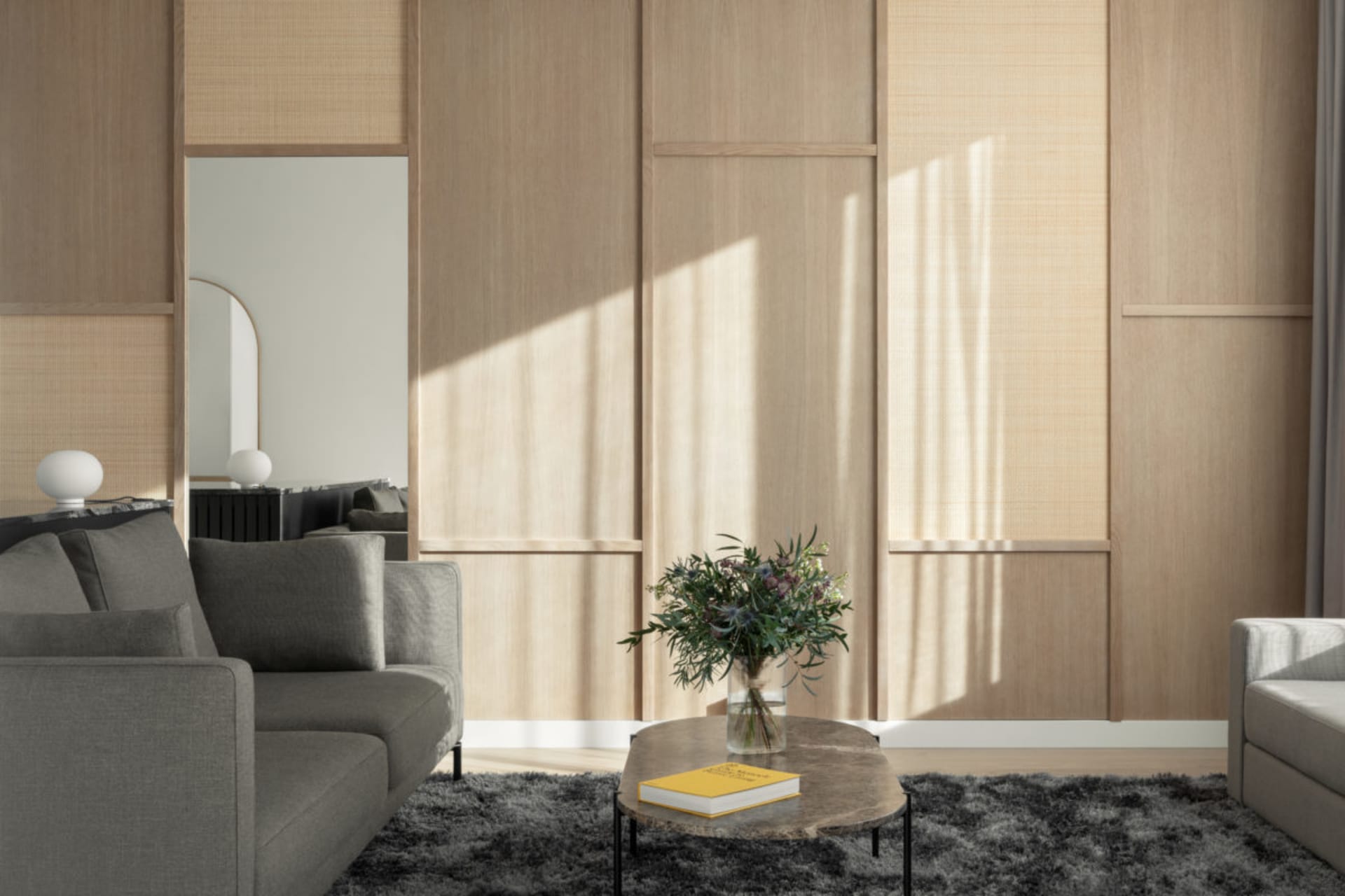 A modern minimalist living room featuring wood paneling, a round coffee table with flowers and a book, and gray sofas.