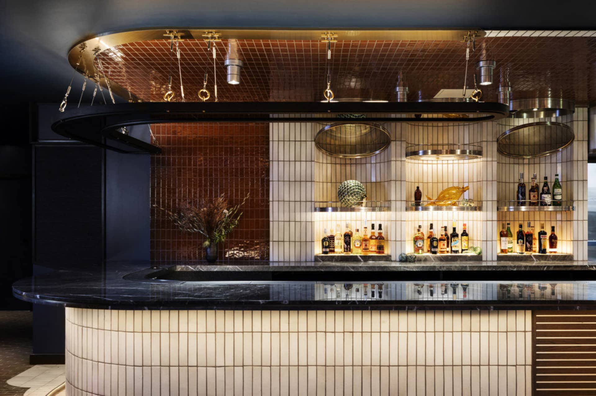 A modern restaurant bar with white and brown marble walls and flooring, featuring a circular hanging light fixture and bottle