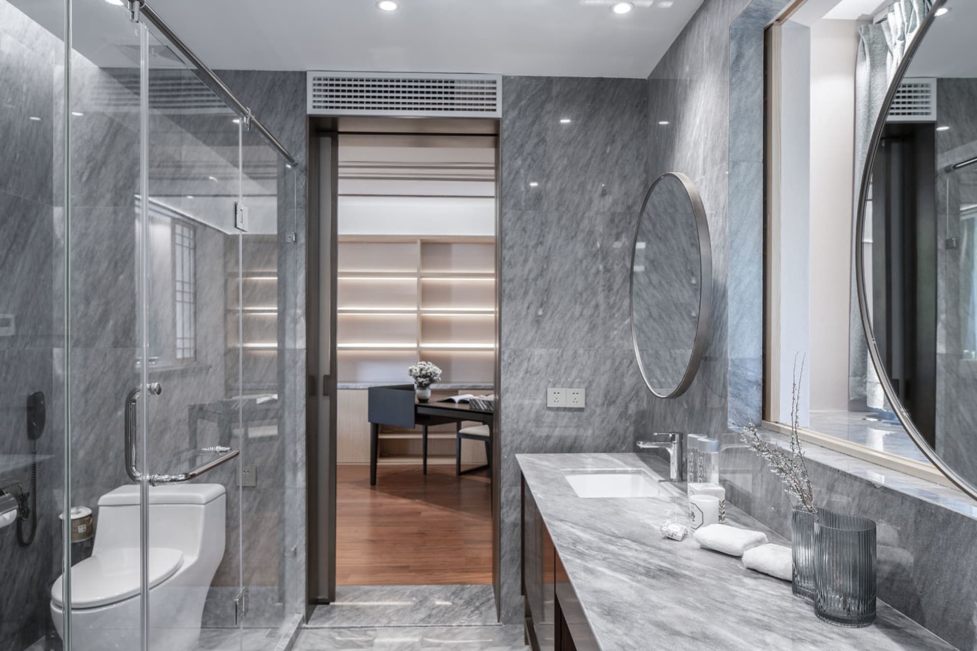 Modern residential bathroom featuring marble walls and flooring, with a glass-enclosed shower and a vanity sink area.