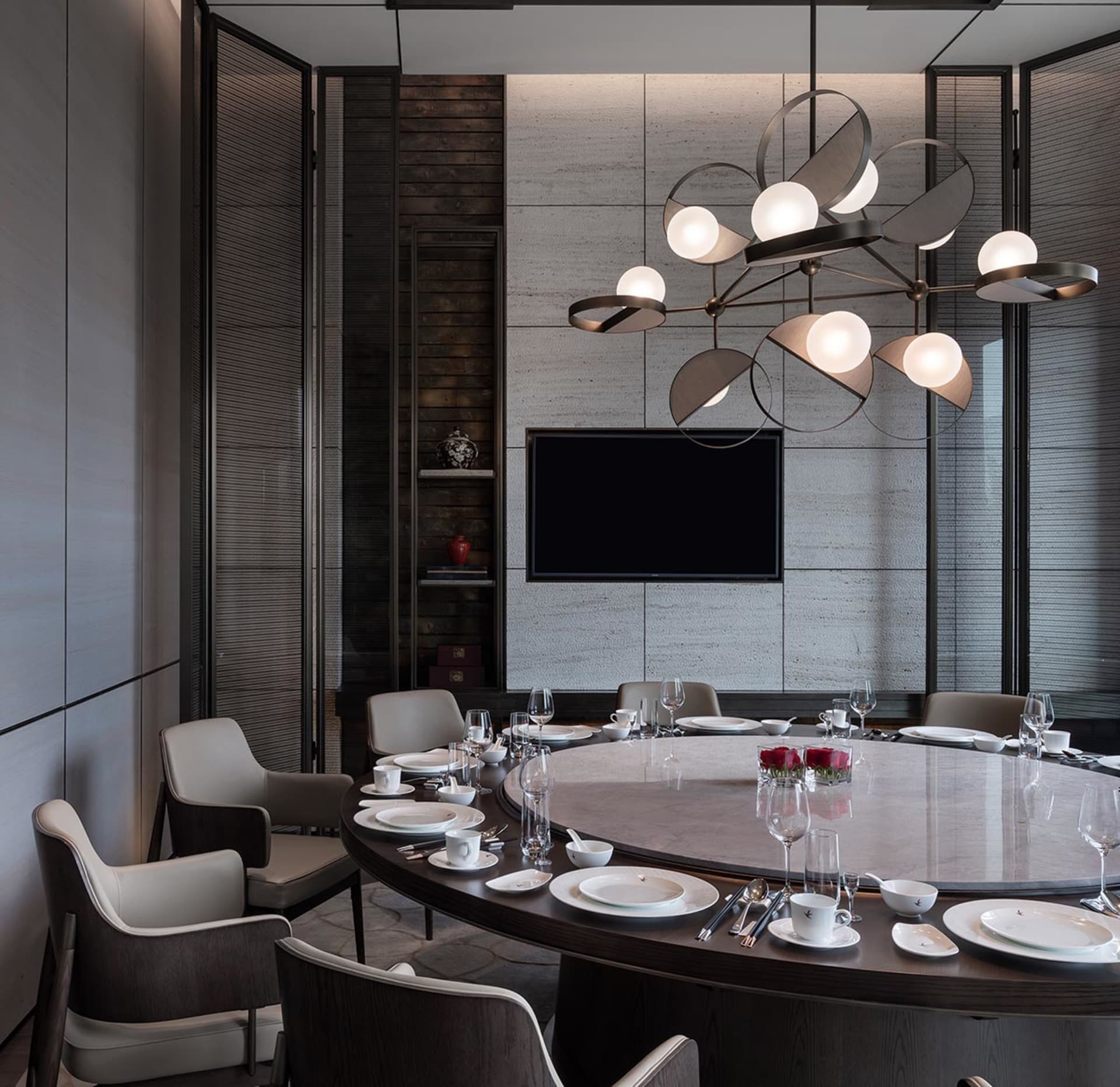 A modern dining room featuring a round table with dishes and glasses, surrounded by white leather chairs, a wooden counter wi
