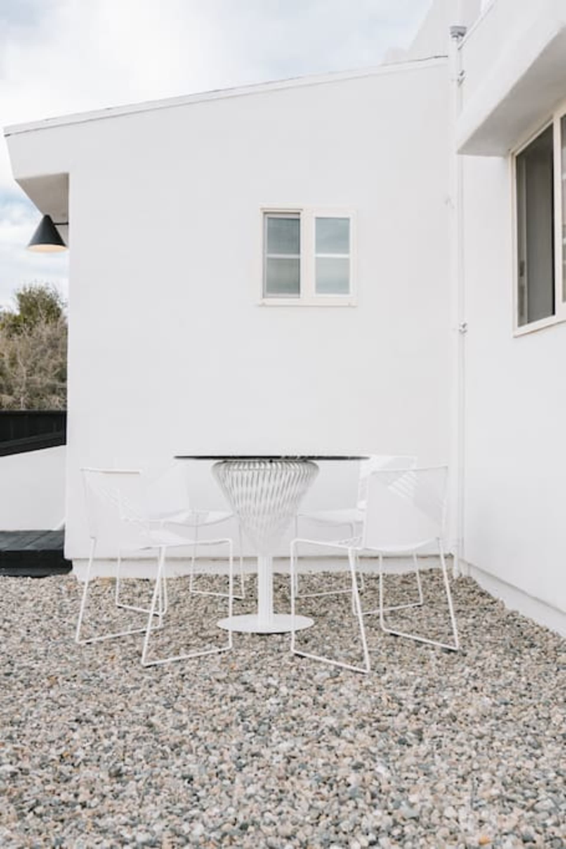 A modern patio featuring a white metal table and chairs on a gravel surface.