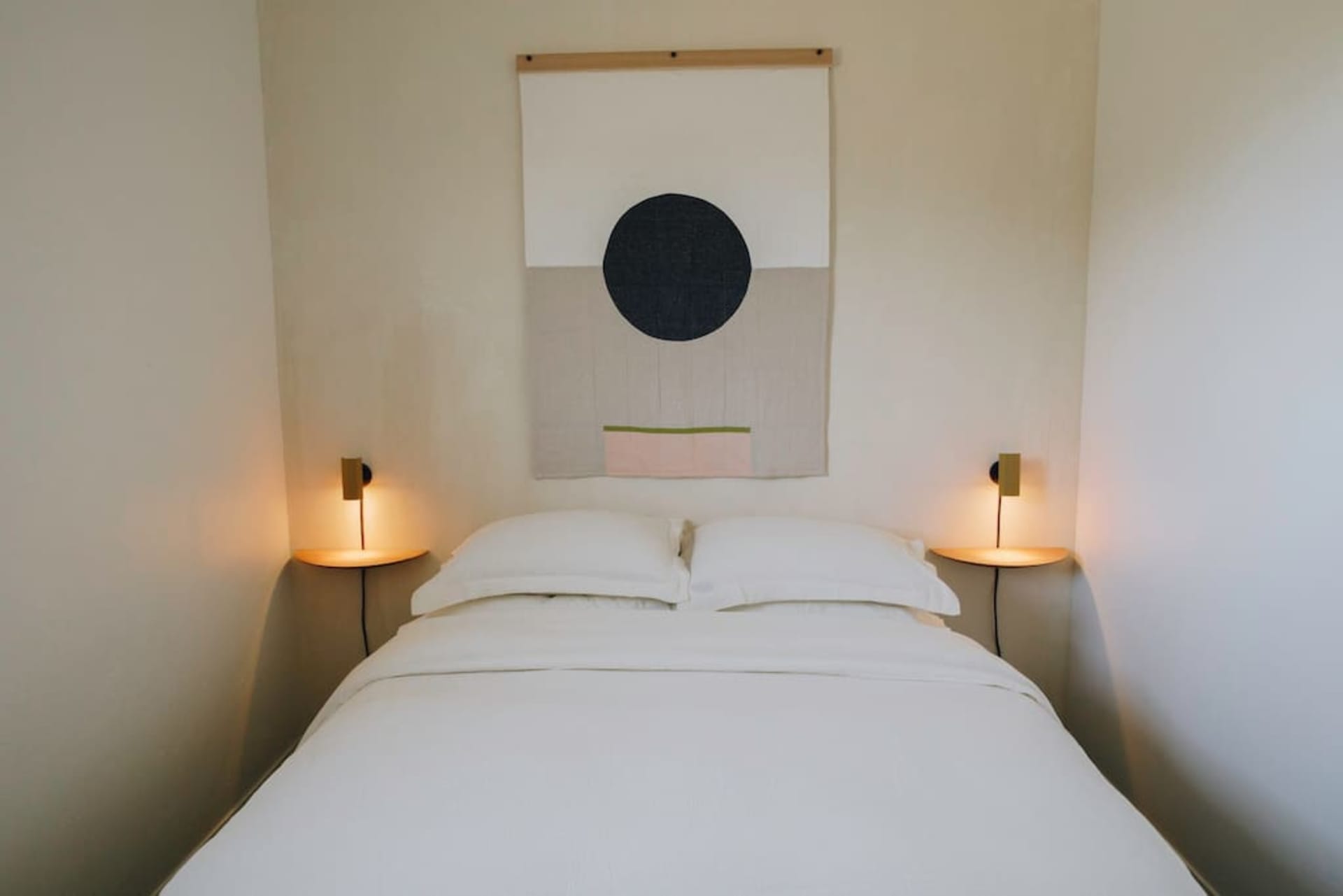 A minimalist bedroom with a white bed, wall sconces, and a geometric wall art