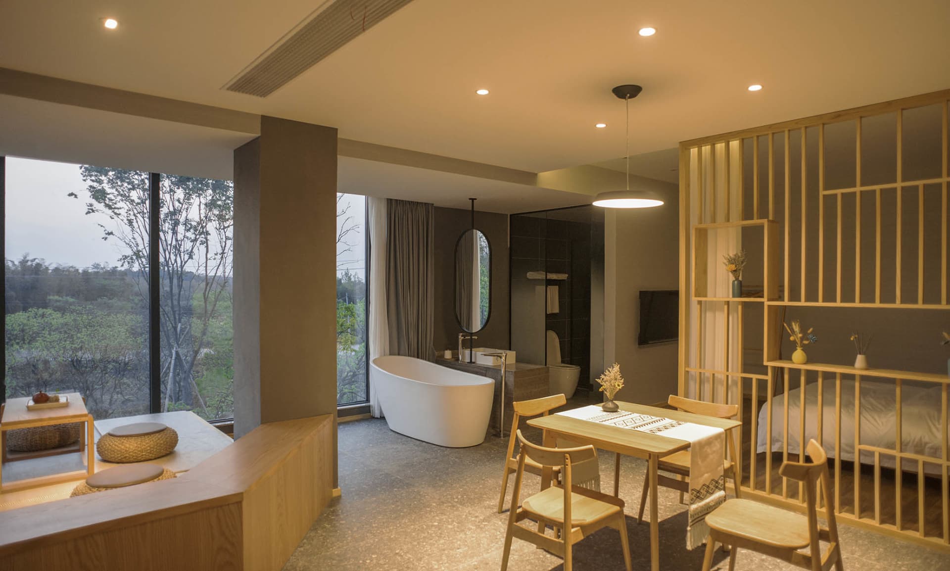 Spacious minimalist residential bathroom with a freestanding bathtub, wooden furniture, and stone flooring.