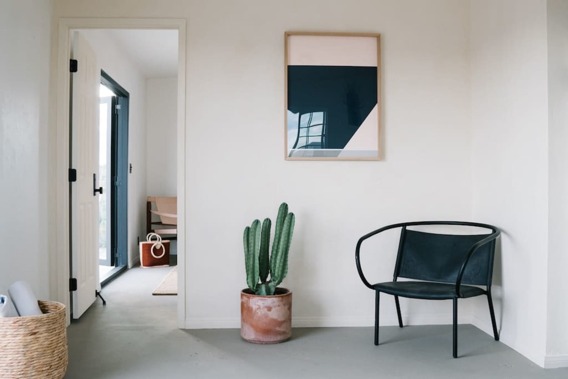 A modern, minimalist interior design featuring concrete elements, a black chair, a cactus plant, and a framed abstract art pi