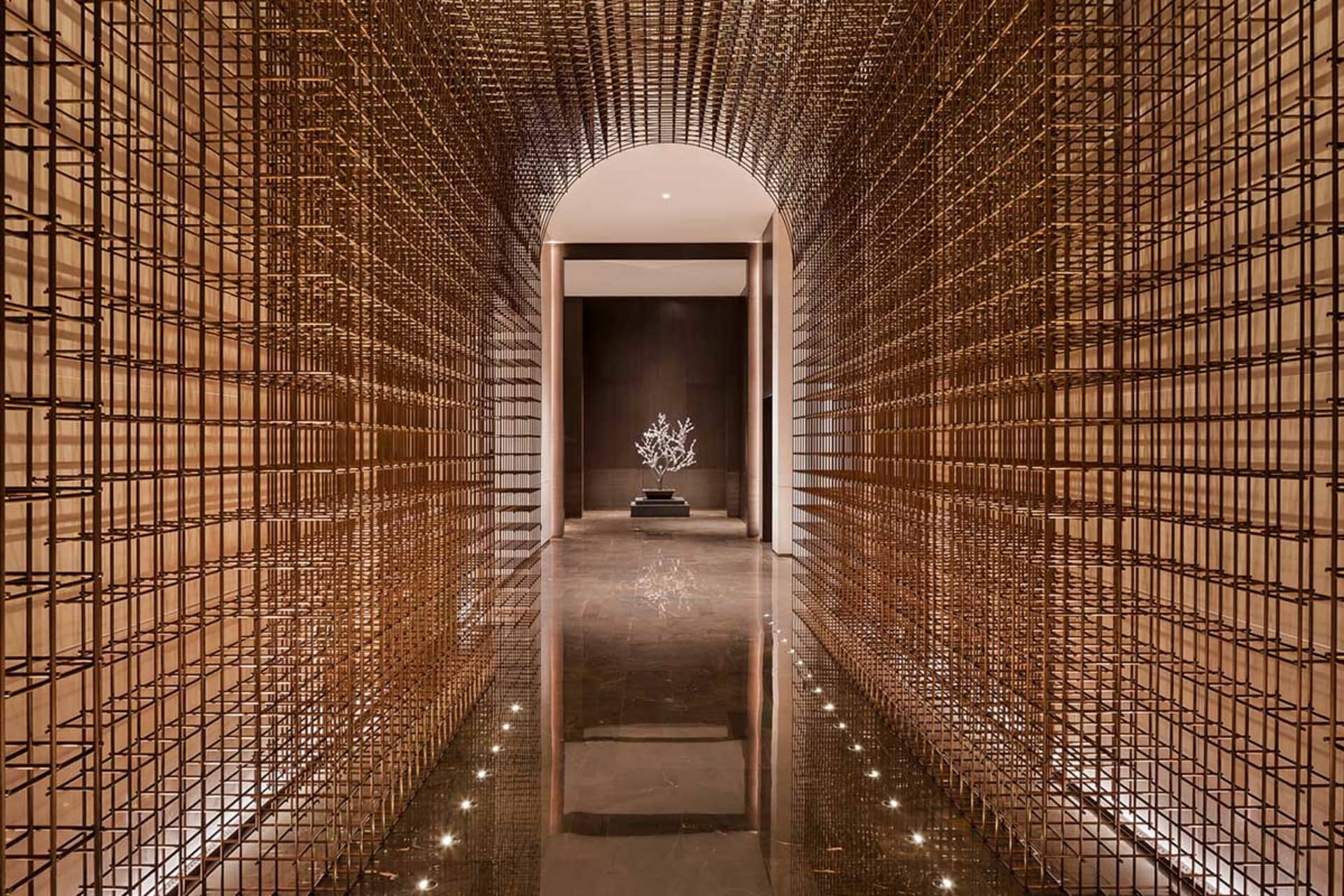 A modern hotel lobby featuring a metal grid wall with a tree sculpture in the center.