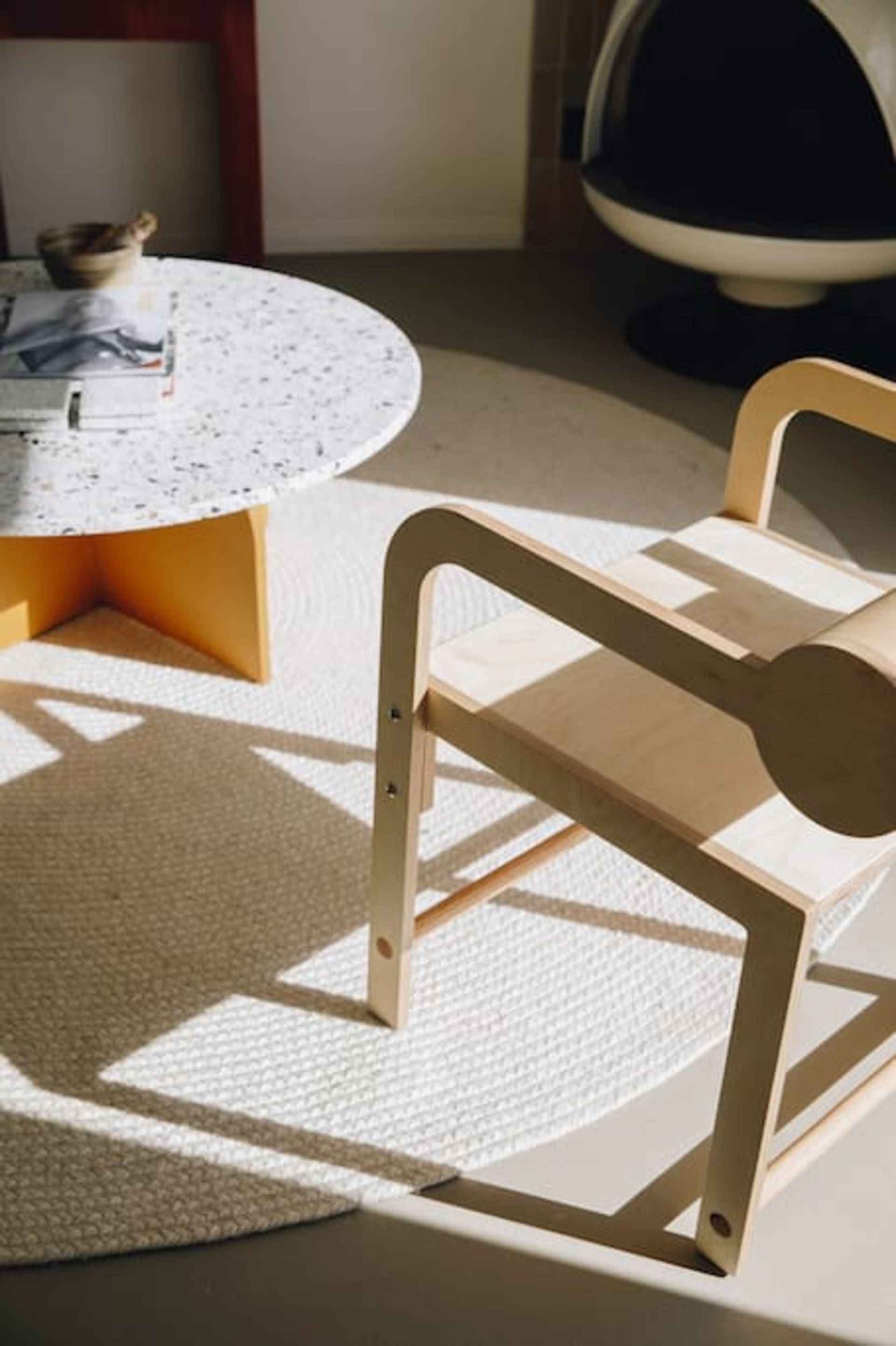 A modern living room with a circular terrazzo coffee table and a minimalist wooden chair.