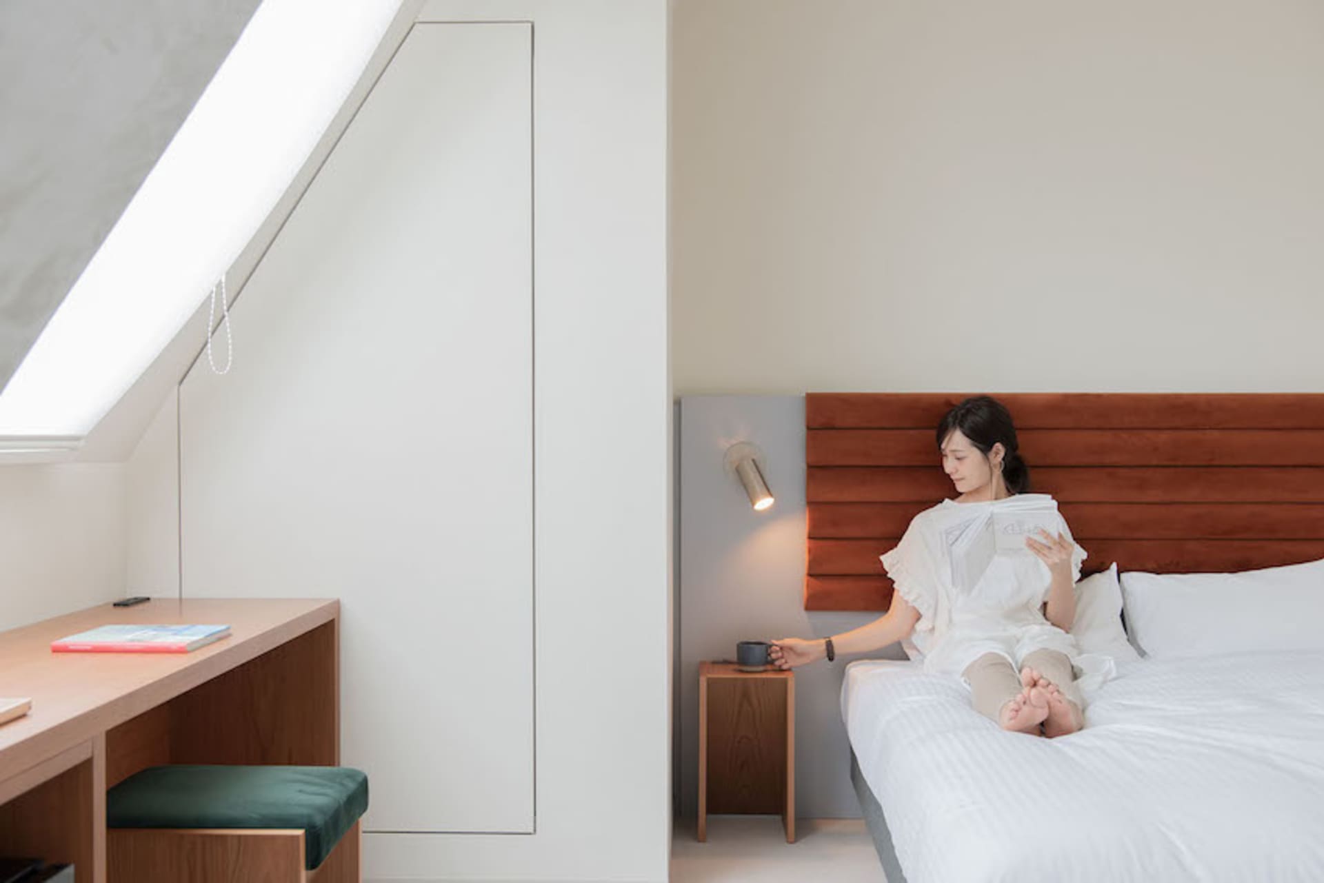 A woman sits on a modern minimalist white bed in a bedroom.