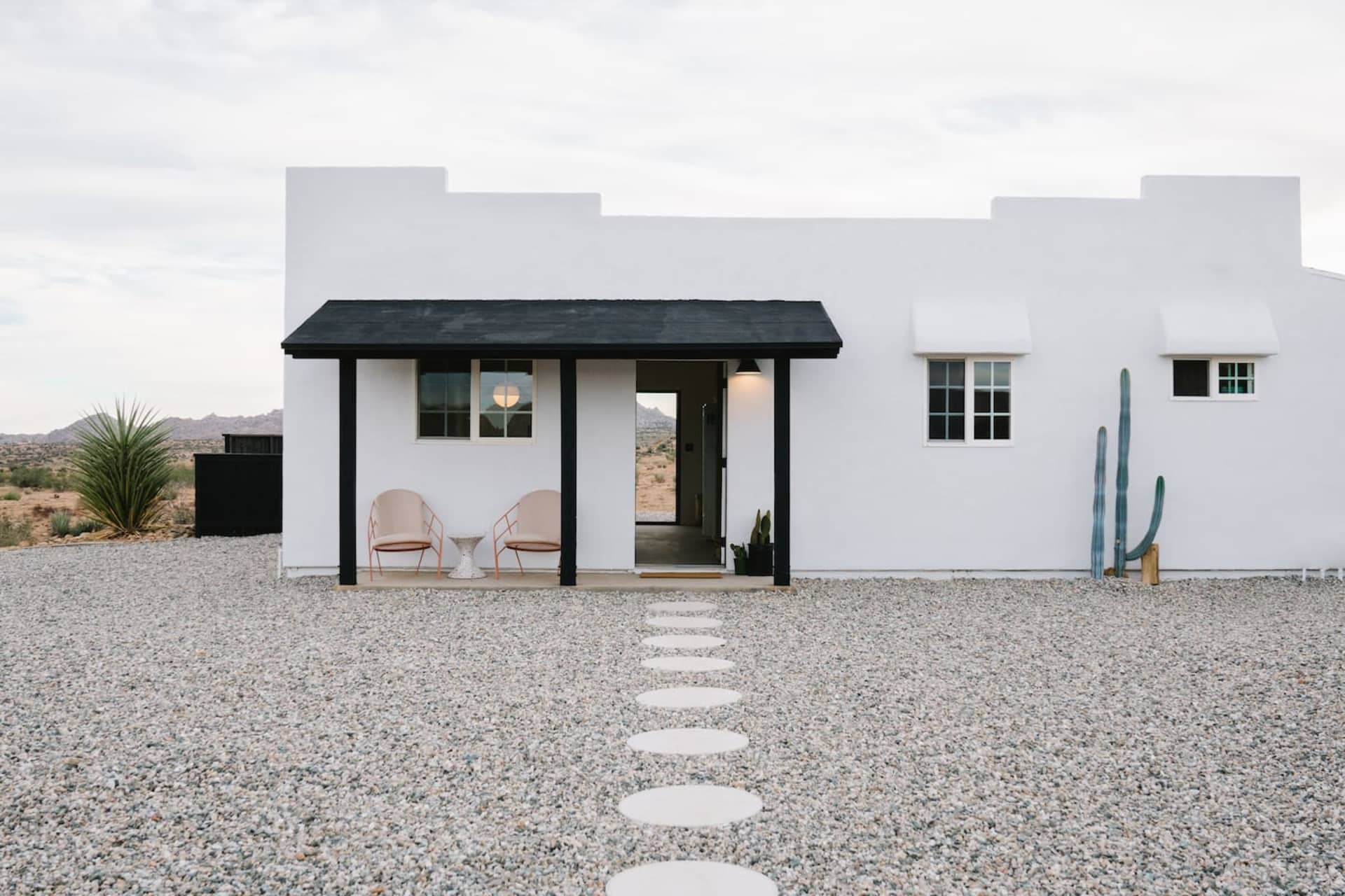 A modern, minimalist house with a white exterior, concrete walkway, and glass windows.