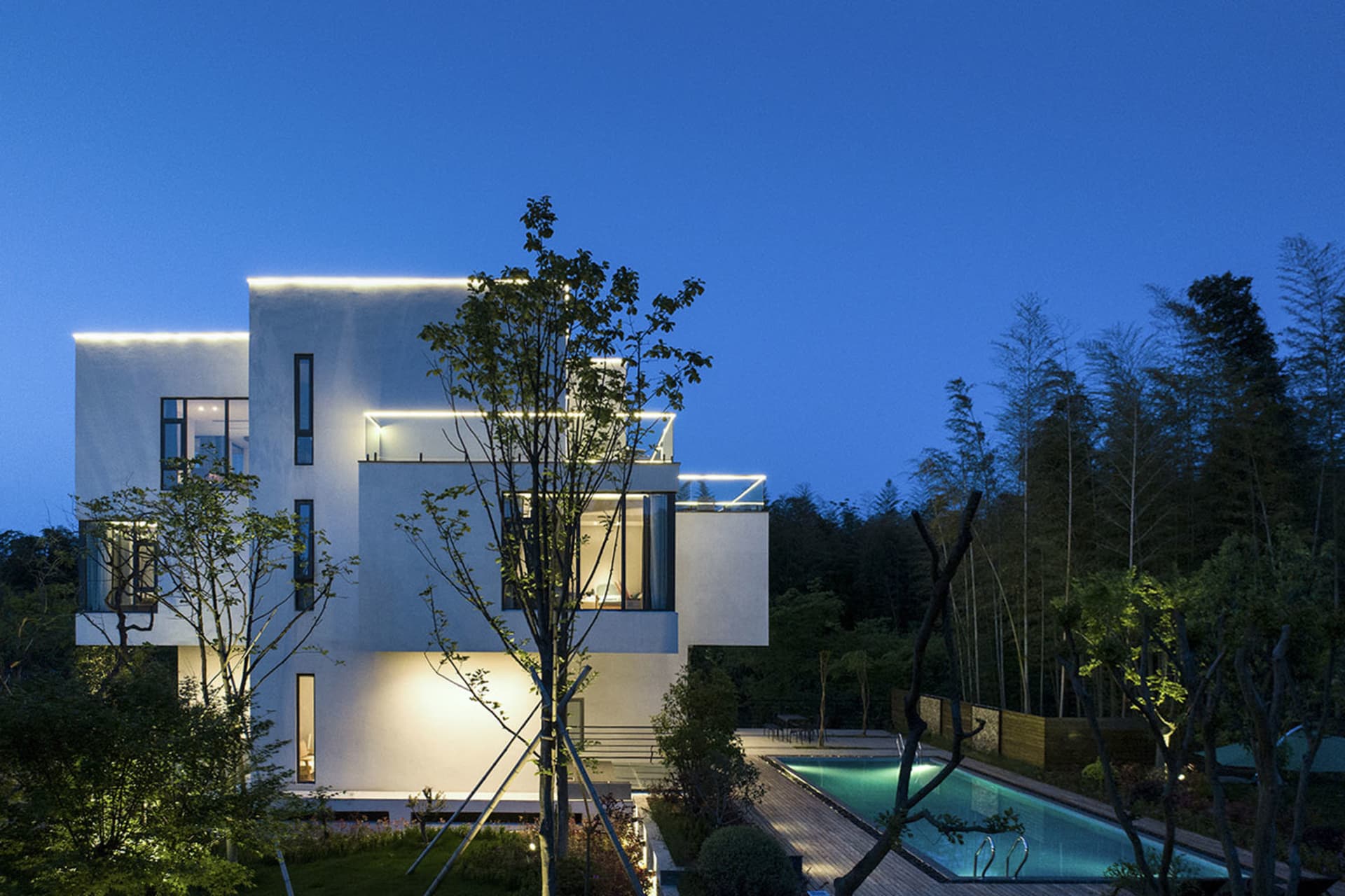 A modern residential building with a white exterior and concrete walls, illuminated at night with warm lights.