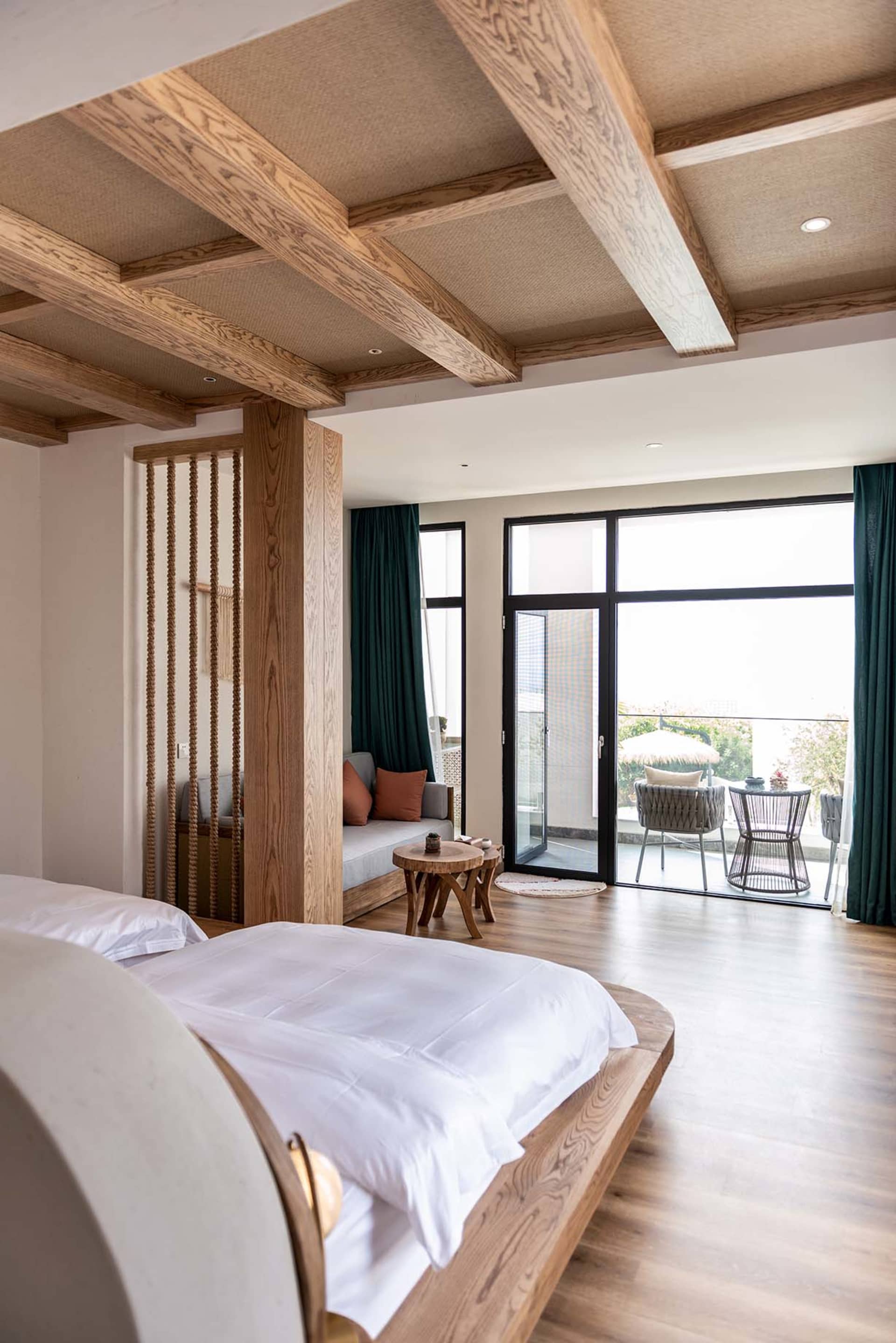 Modern bedroom with a white bed, wooden furniture, and a view of a balcony with chairs and a table.