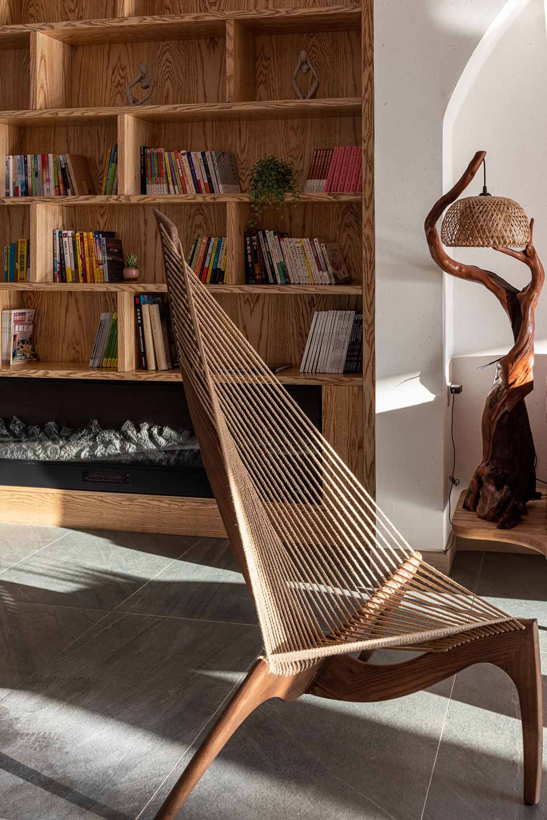 Modern, minimalist lounge area with wooden furniture, a bookshelf, a unique floor lamp, and a cozy atmosphere.