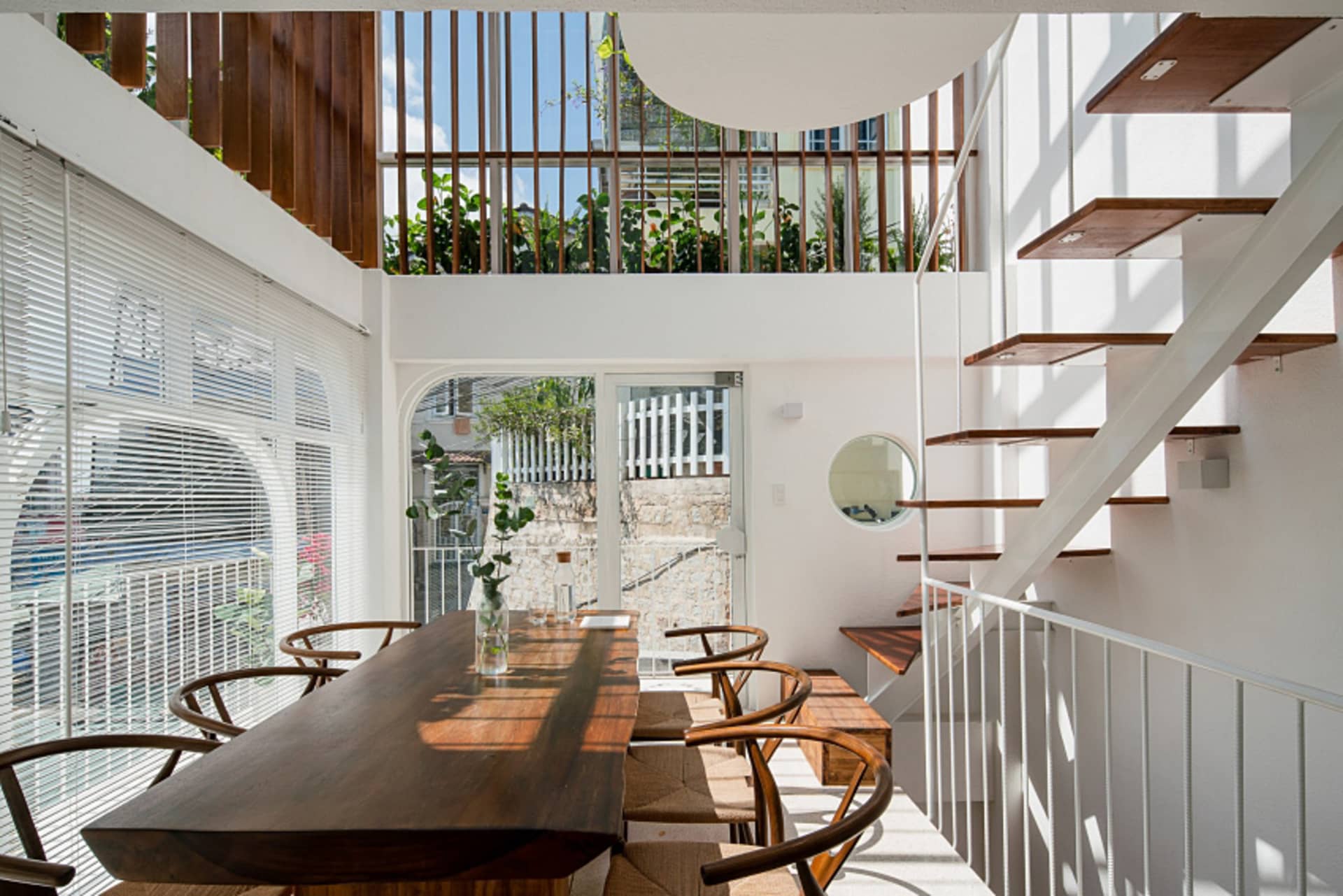A modern indoor living space featuring a wooden dining table, glass walls, and a concrete staircase.