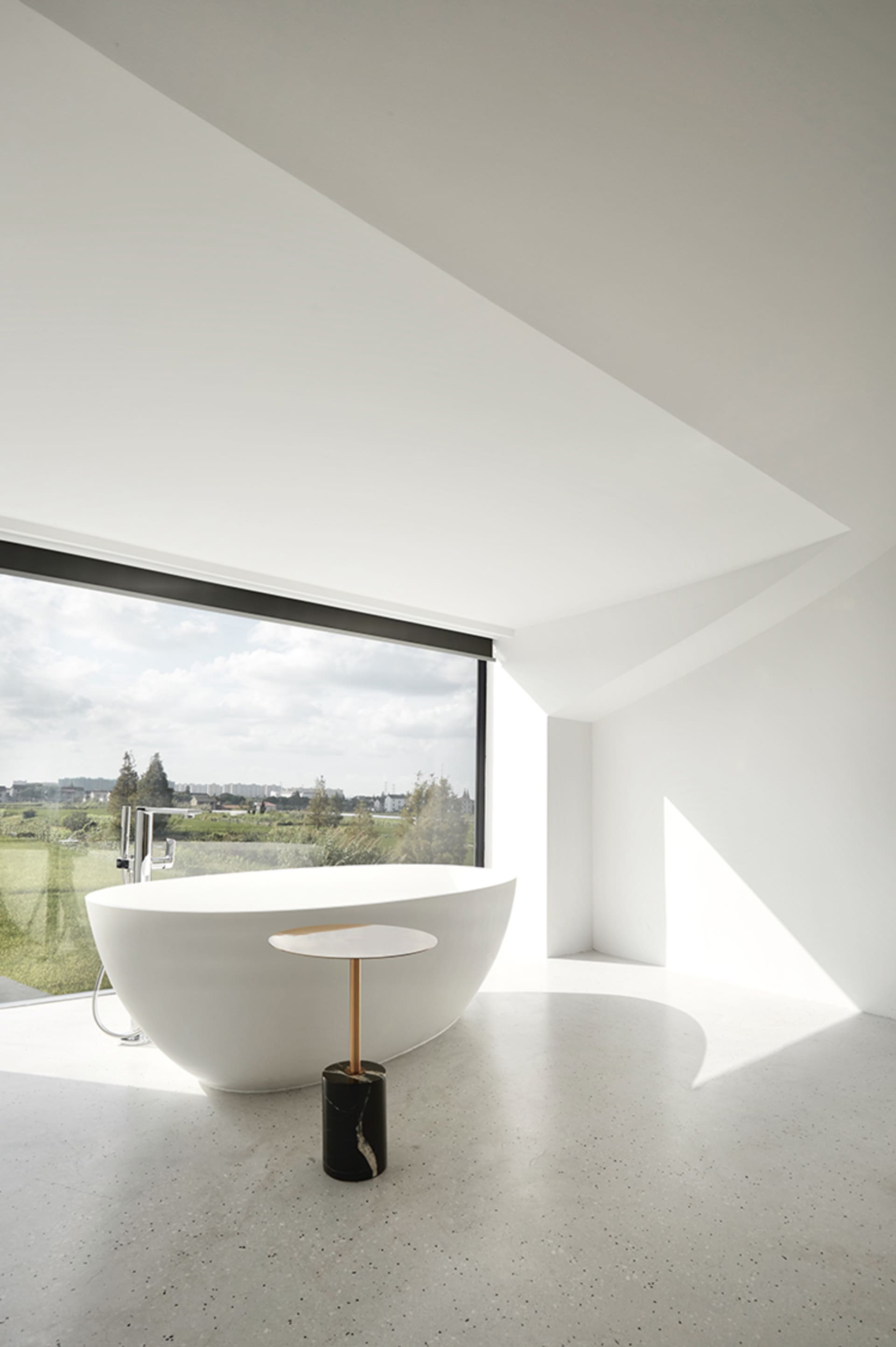 A minimalist bathroom with a freestanding white bathtub, a black and white marble table, and a large window with a view of th