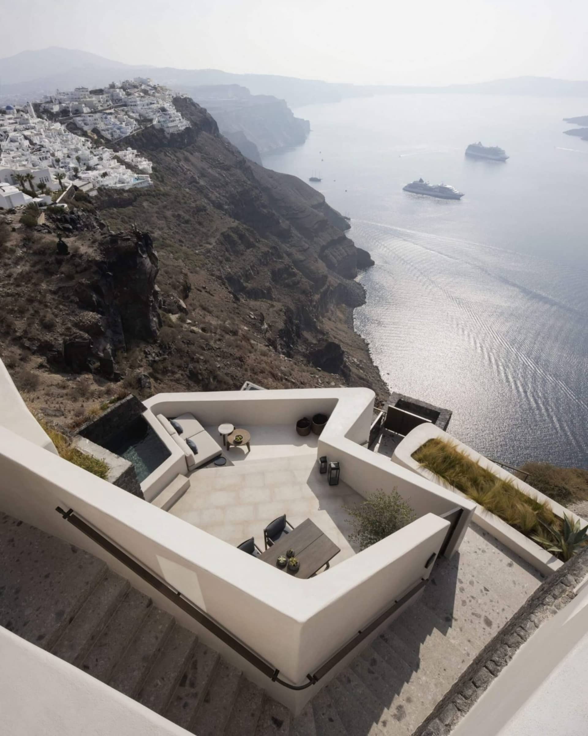 An outdoor seating area designed with a minimalist aesthetic, featuring concrete furniture and a view of the sea.