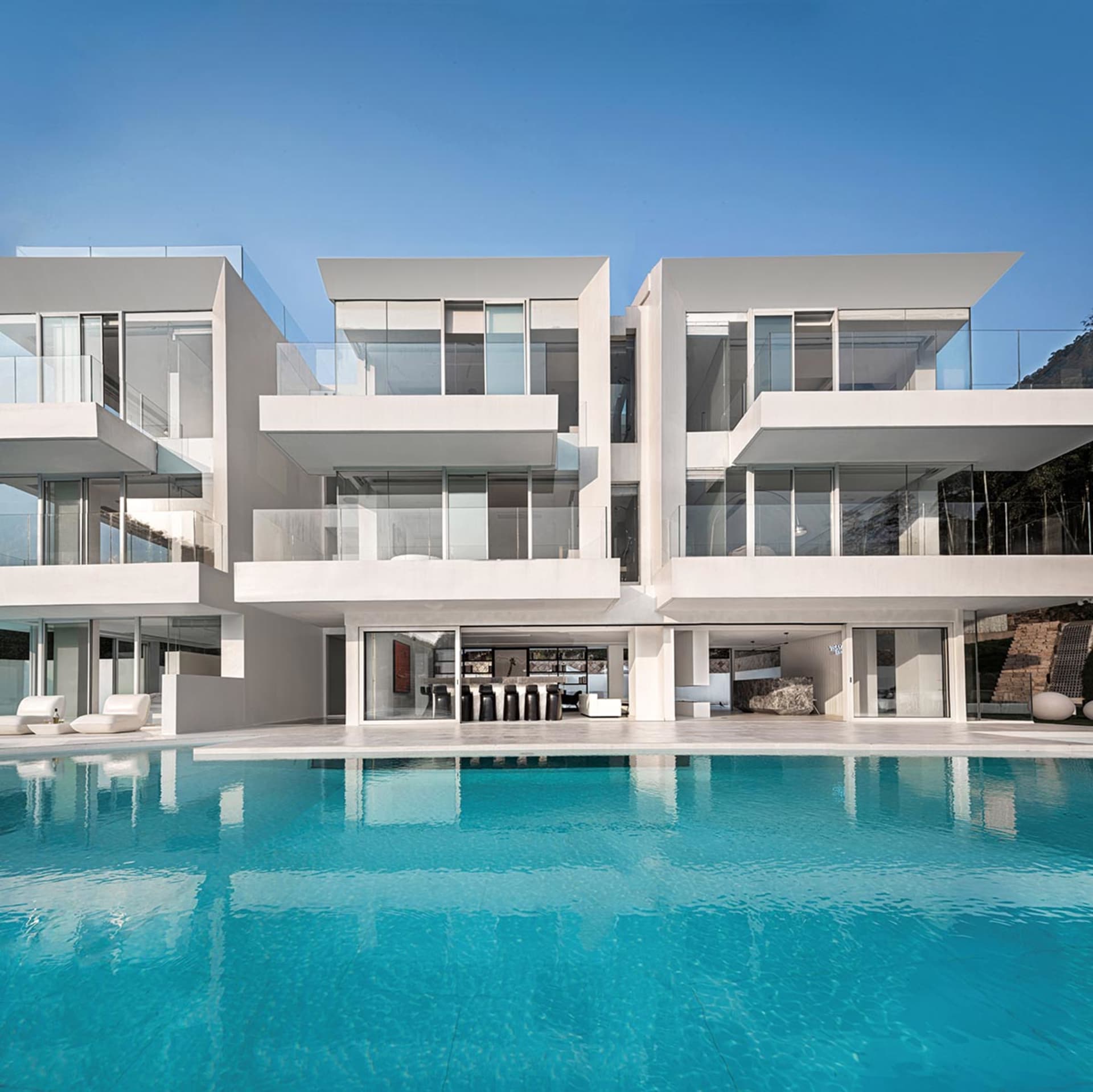 A modern residential pool house featuring white stone and glass exterior materials.