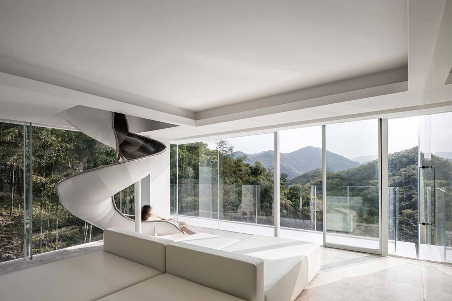 Modern white leather and glass living room with spiral staircase and floor-to-ceiling windows overlooking mountains.