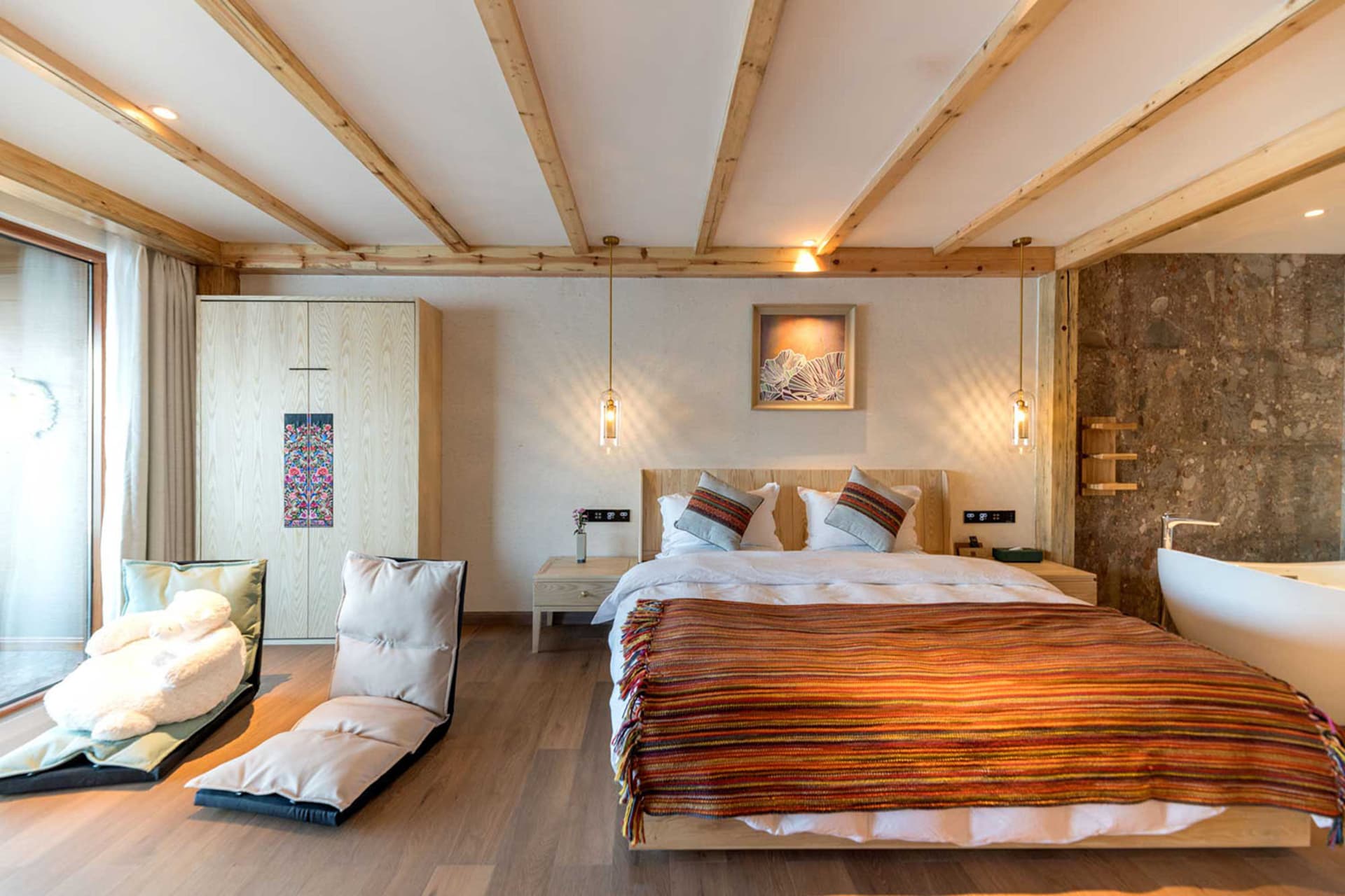 Minimalist bedroom featuring wood and stone materials, with a large bed, colorful blanket, and a bathtub.