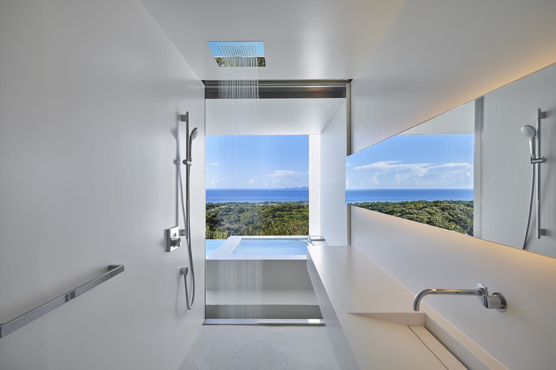Modern minimalist bathroom with glass shower walls overlooking a scenic ocean view.