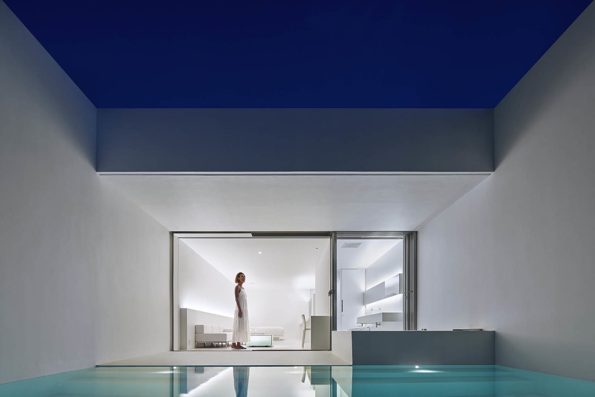 A modern living room with a minimalist design, featuring exposed concrete walls and a large glass window.