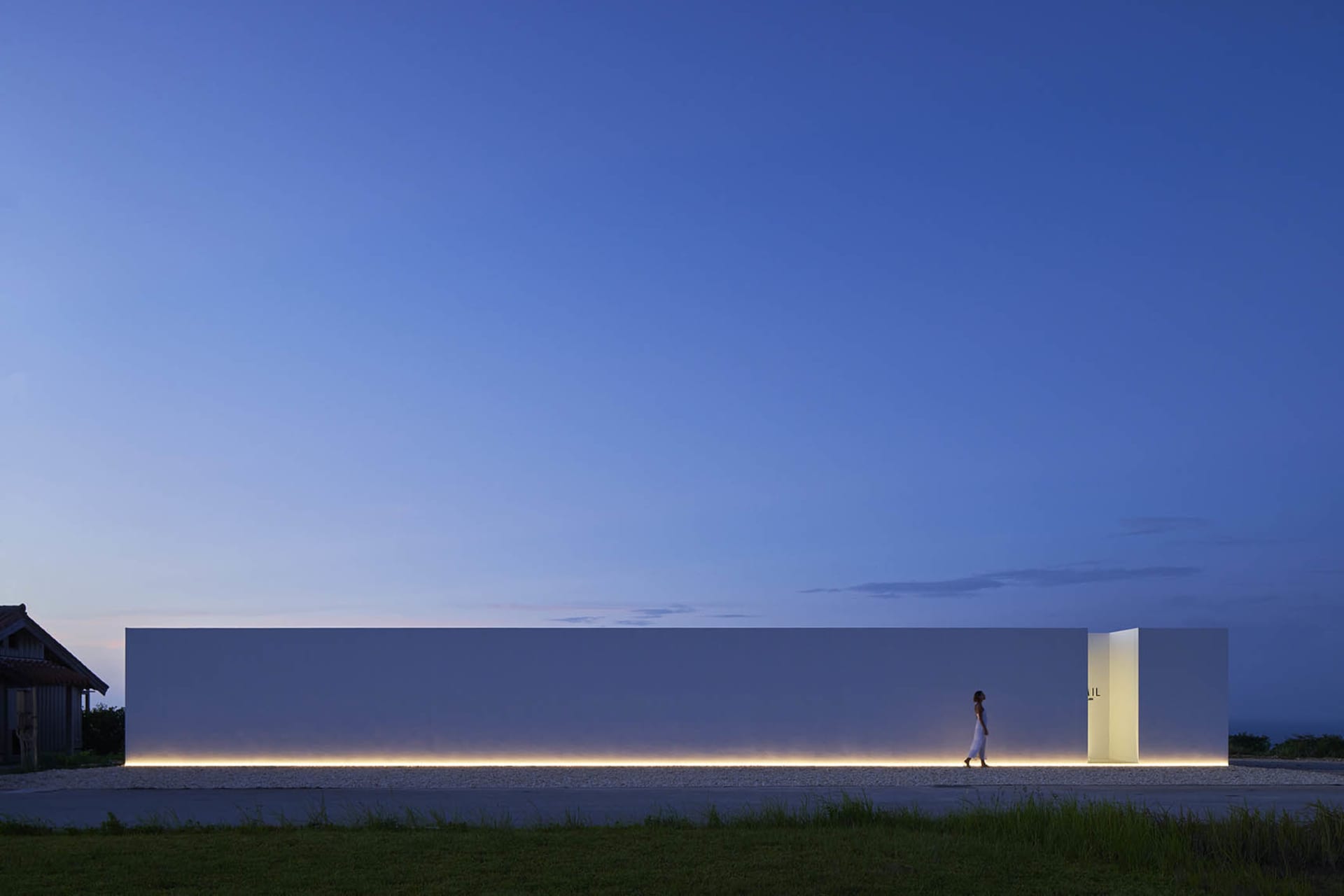 Modern exterior building with a white facade and concrete construction, illuminated by ambient lighting against a twilight sk