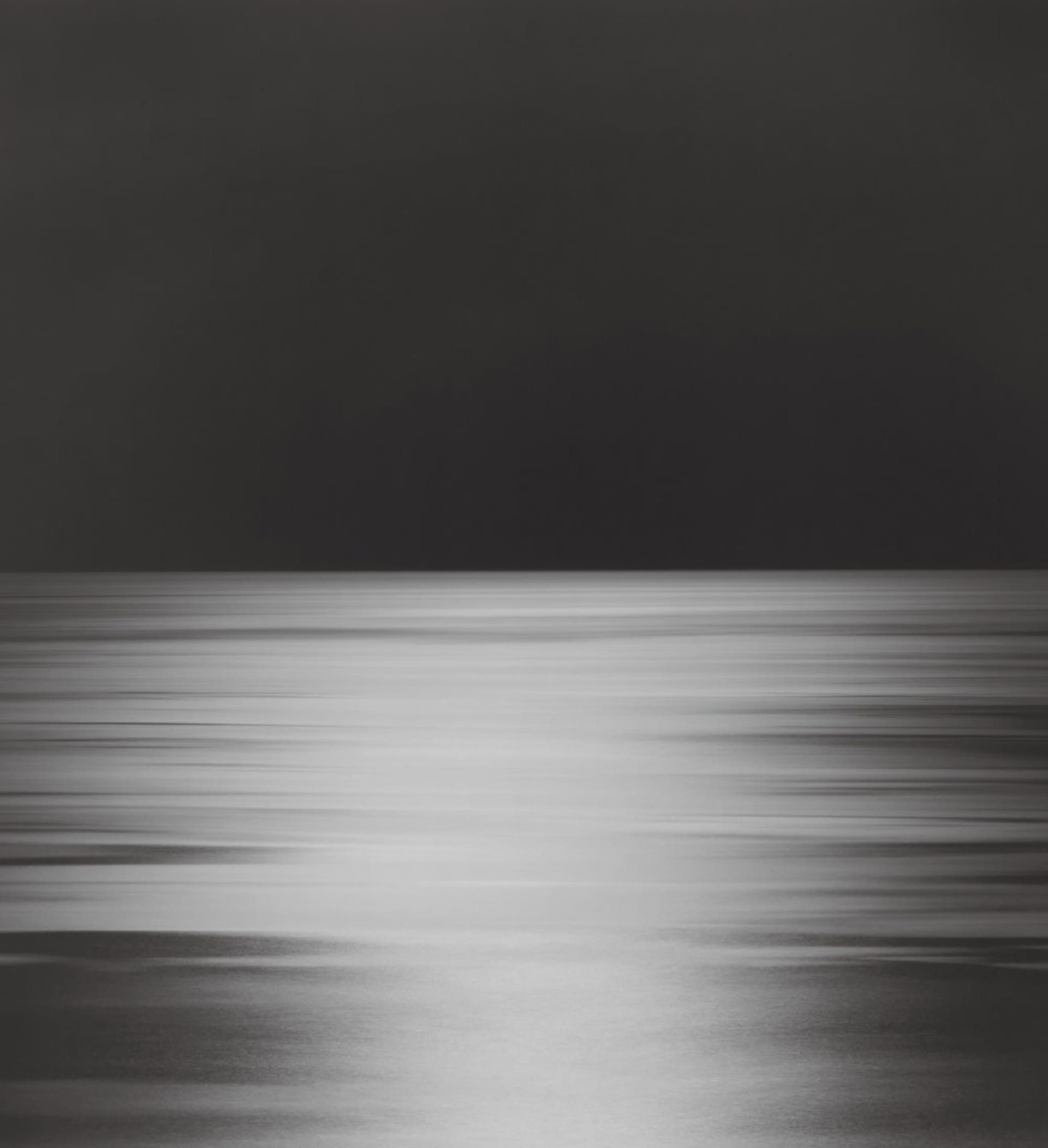 A black and white photograph of a blurred ocean scene at night