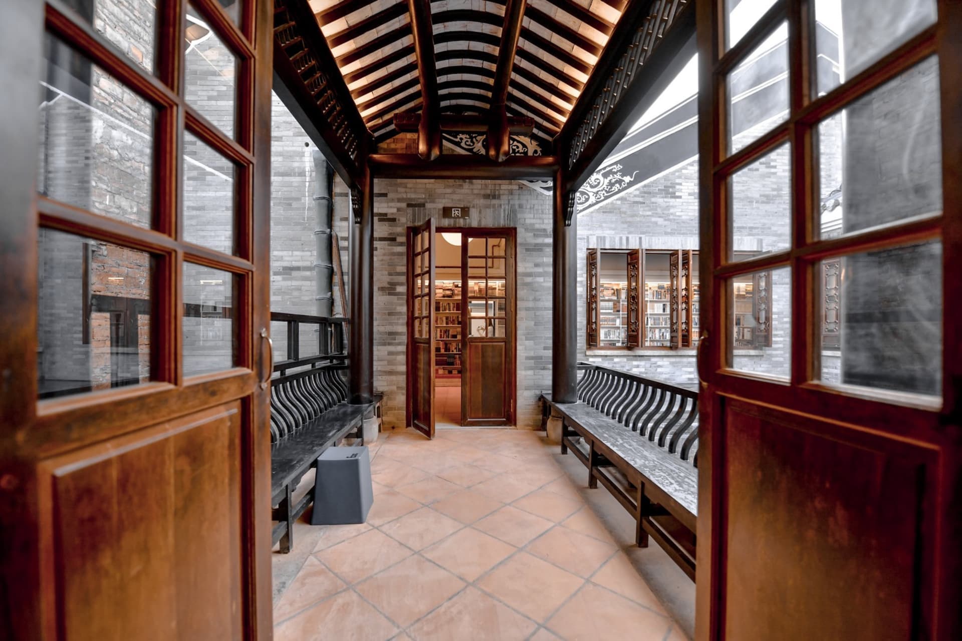 An open doorway into a library with wooden benches and shelves filled with books.