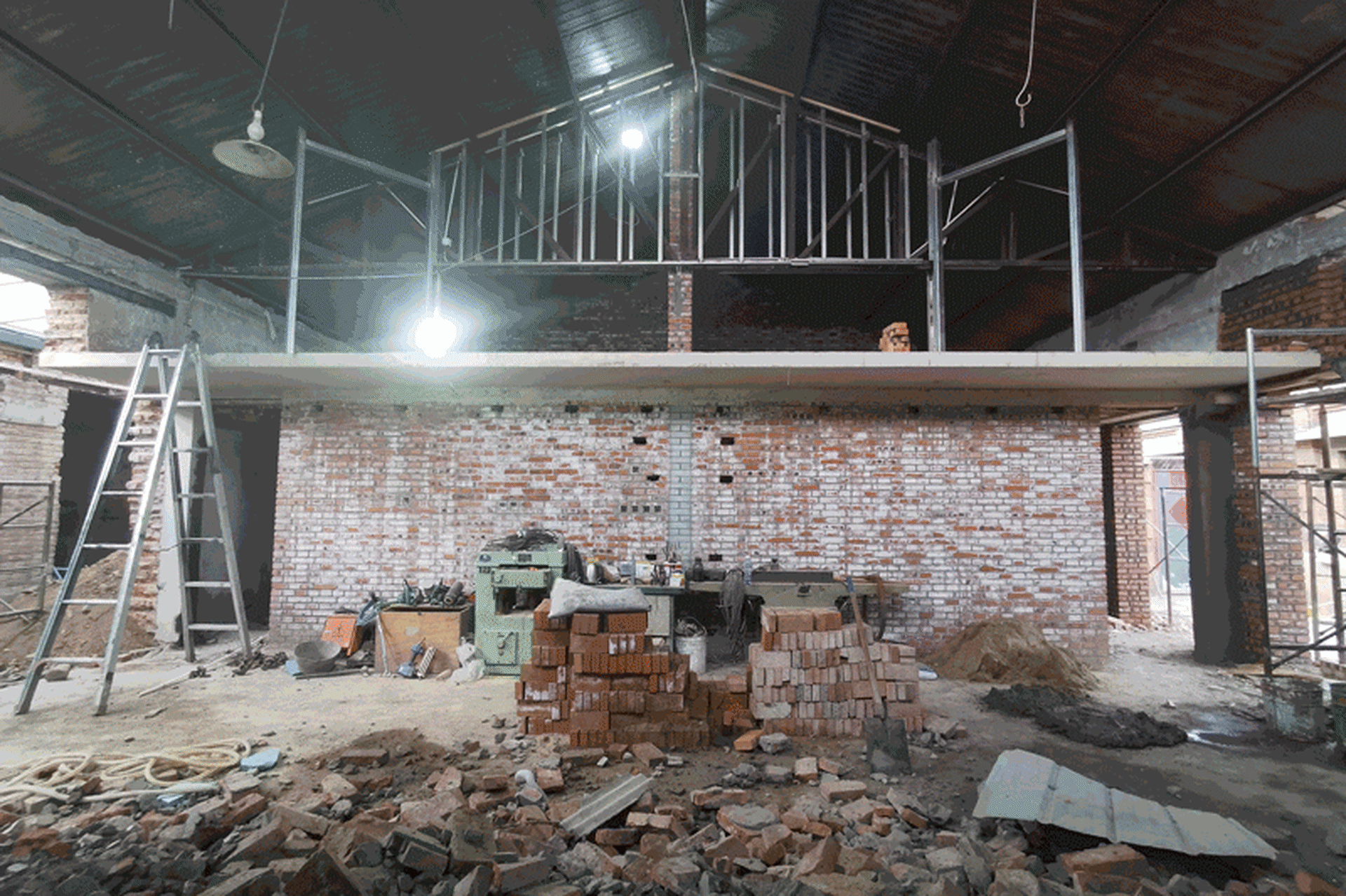 A construction site with exposed brick, concrete, aluminum framing, and a high beam roof structure.