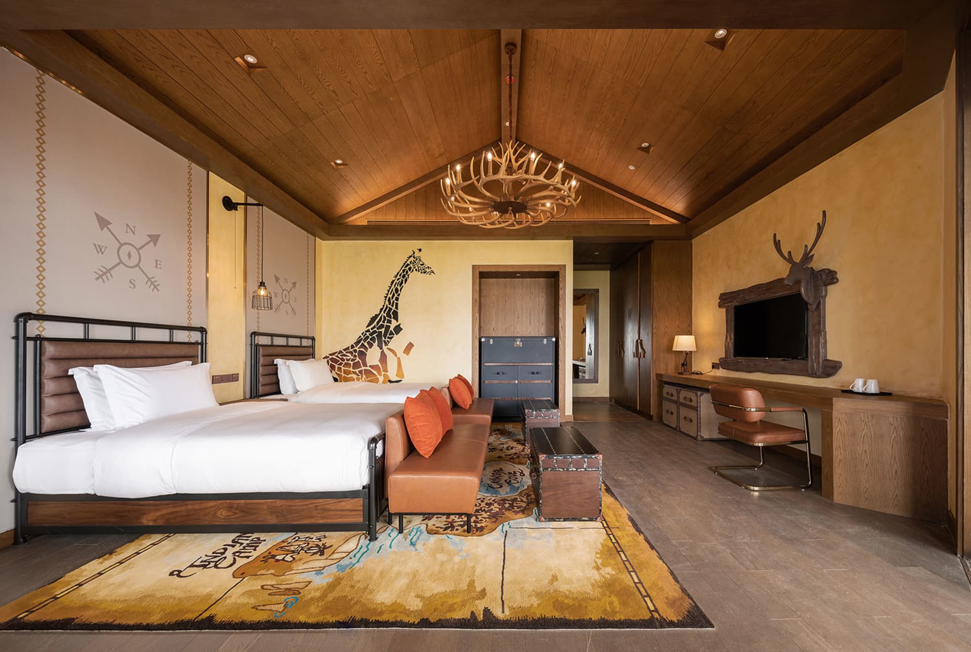 Modern hotel room featuring wood-themed decor and furniture, including a bed, sofa, desk, and chandelier.