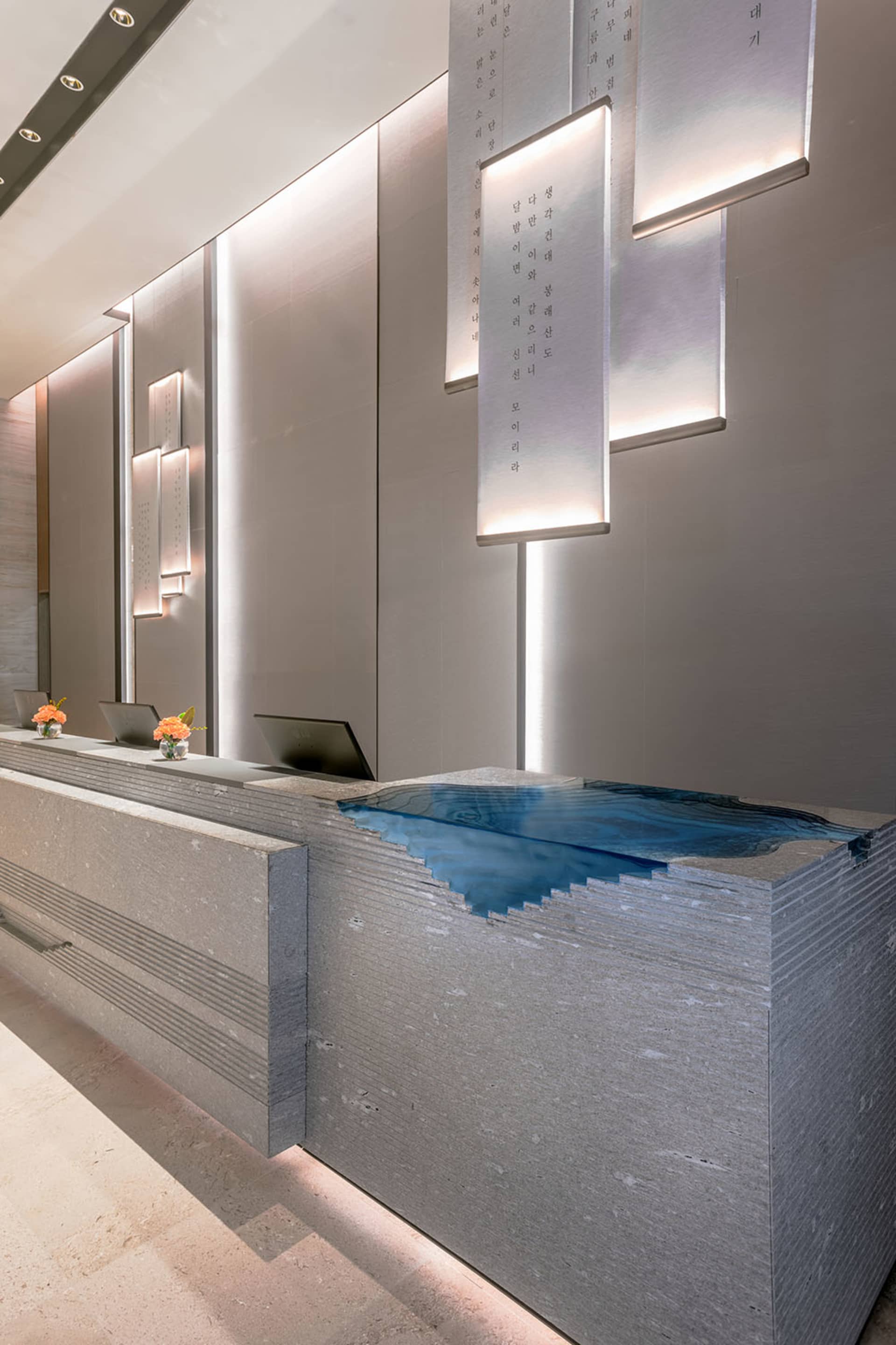 A minimalist reception desk made of concrete with a blue water feature.