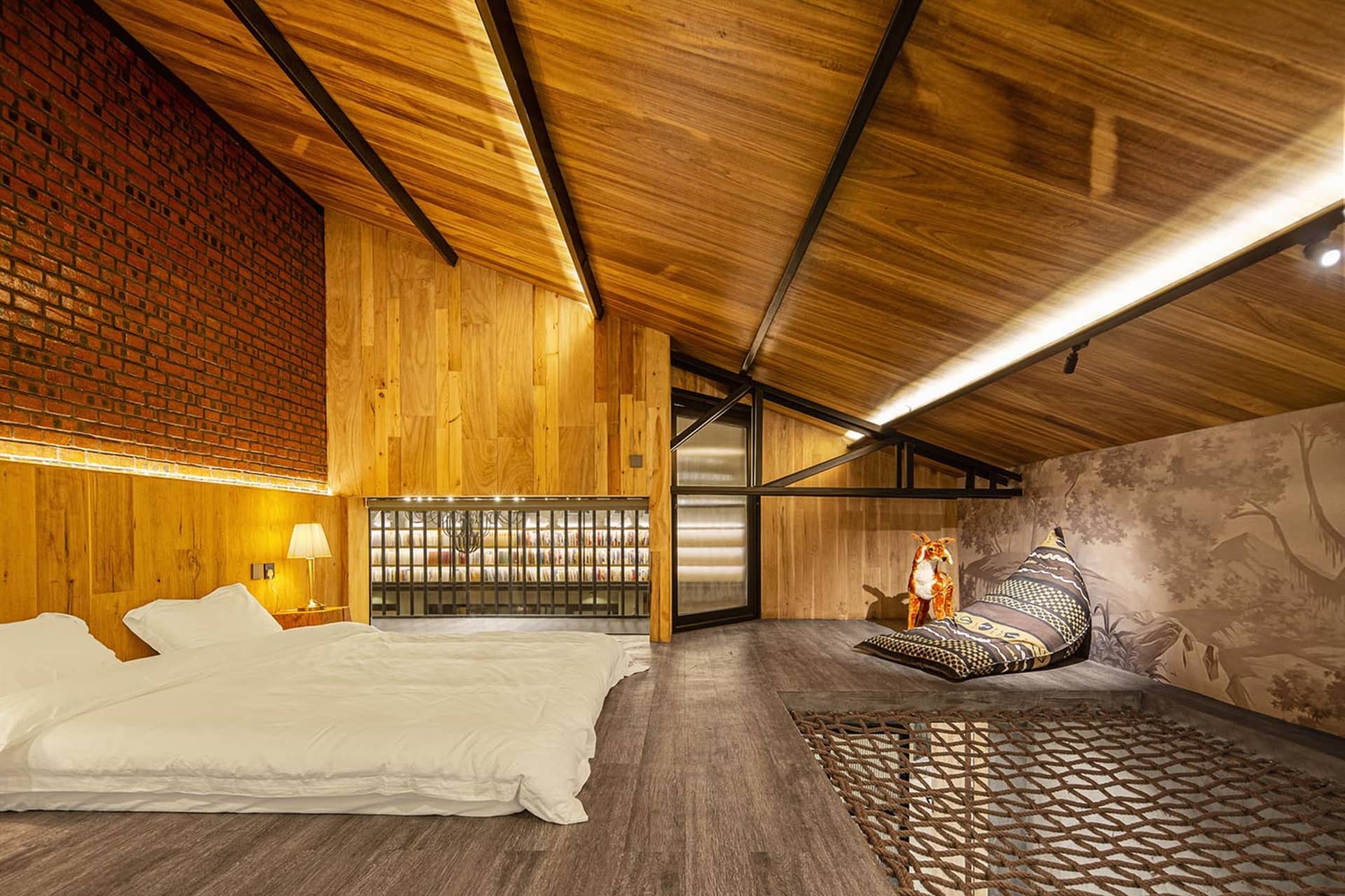 Modern bedroom with wooden walls, floor, and ceiling, featuring a bed and a cozy sitting area with a pillow and a fox figurin