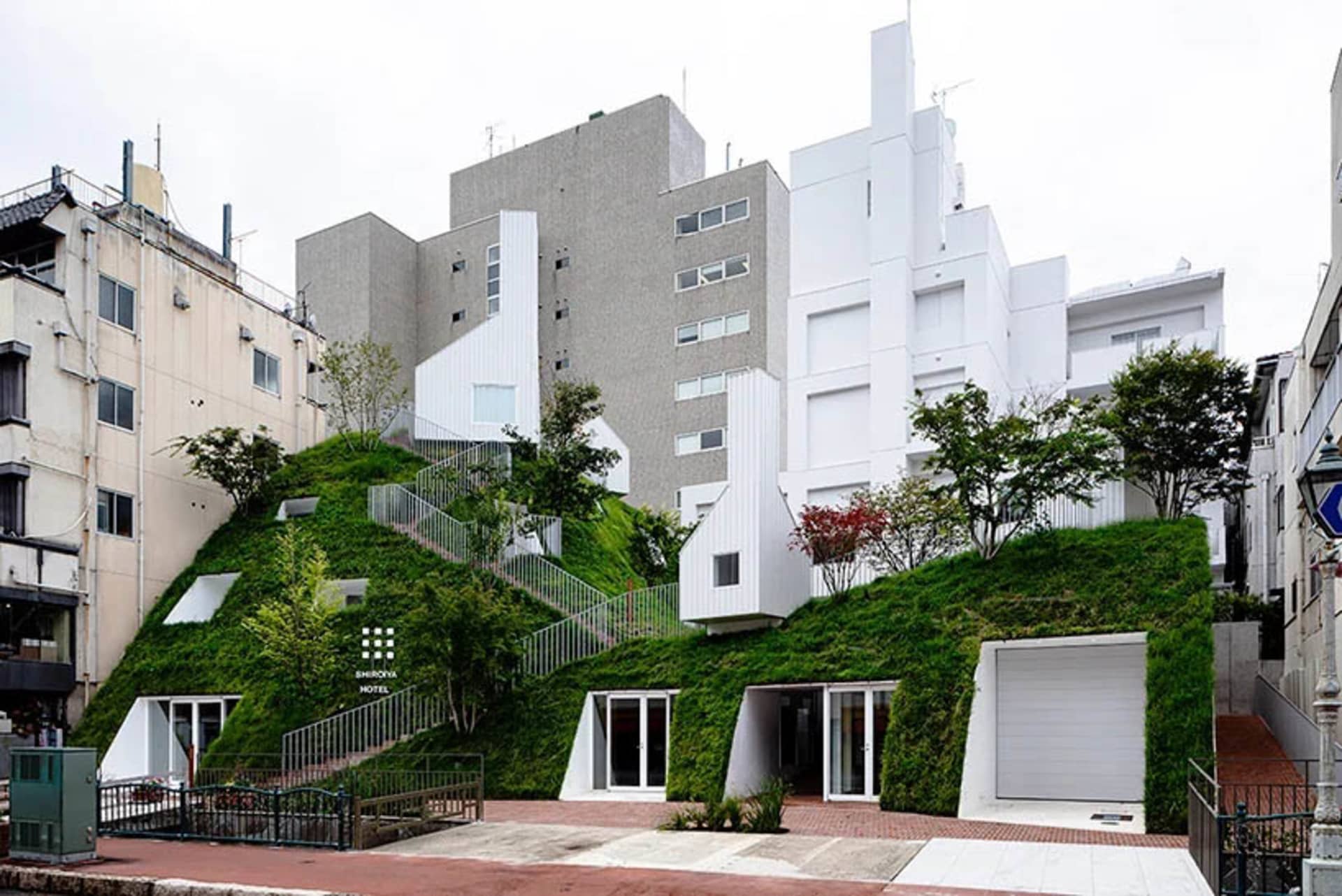 一座現代住宅大樓，擁有綠色屋頂，周圍環繞綠意與其他建築物。