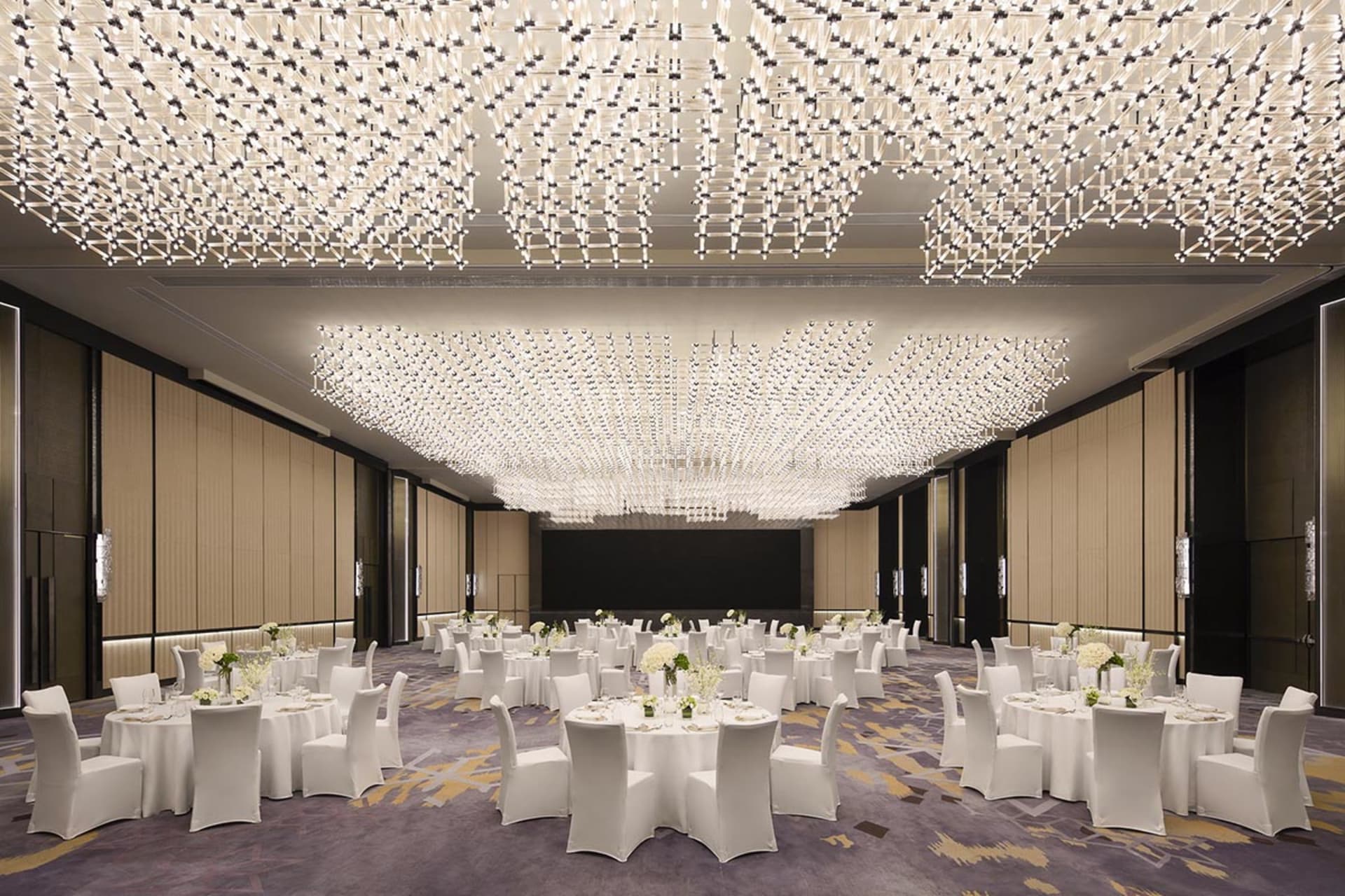 A modern banquet hall with white lighting and white tables and chairs.