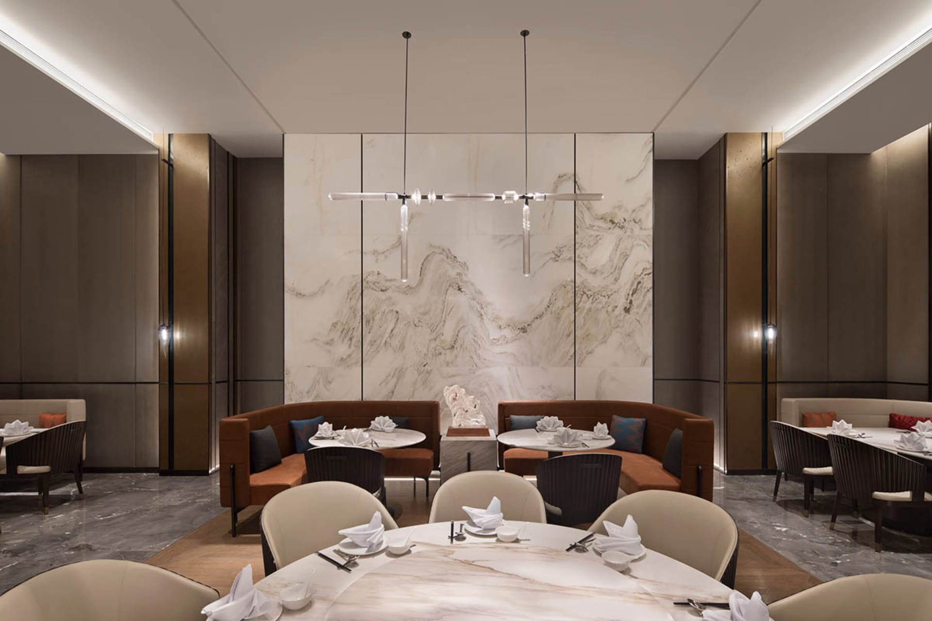 A modern restaurant interior featuring a large marble wall, round dining tables, and comfortable seating areas.
