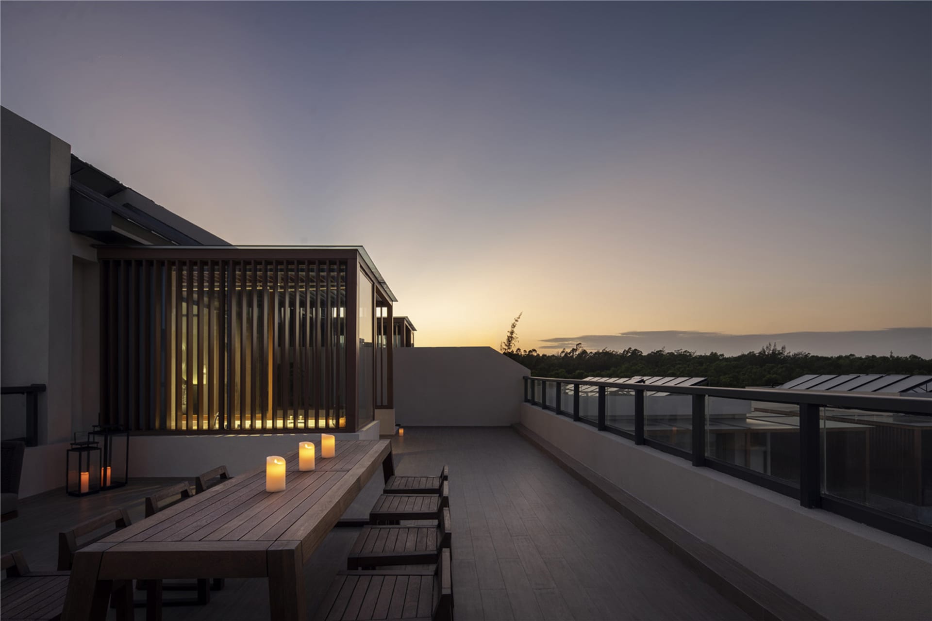 Outdoor residential space at dusk with minimalist design featuring wood, glass, and metal elements