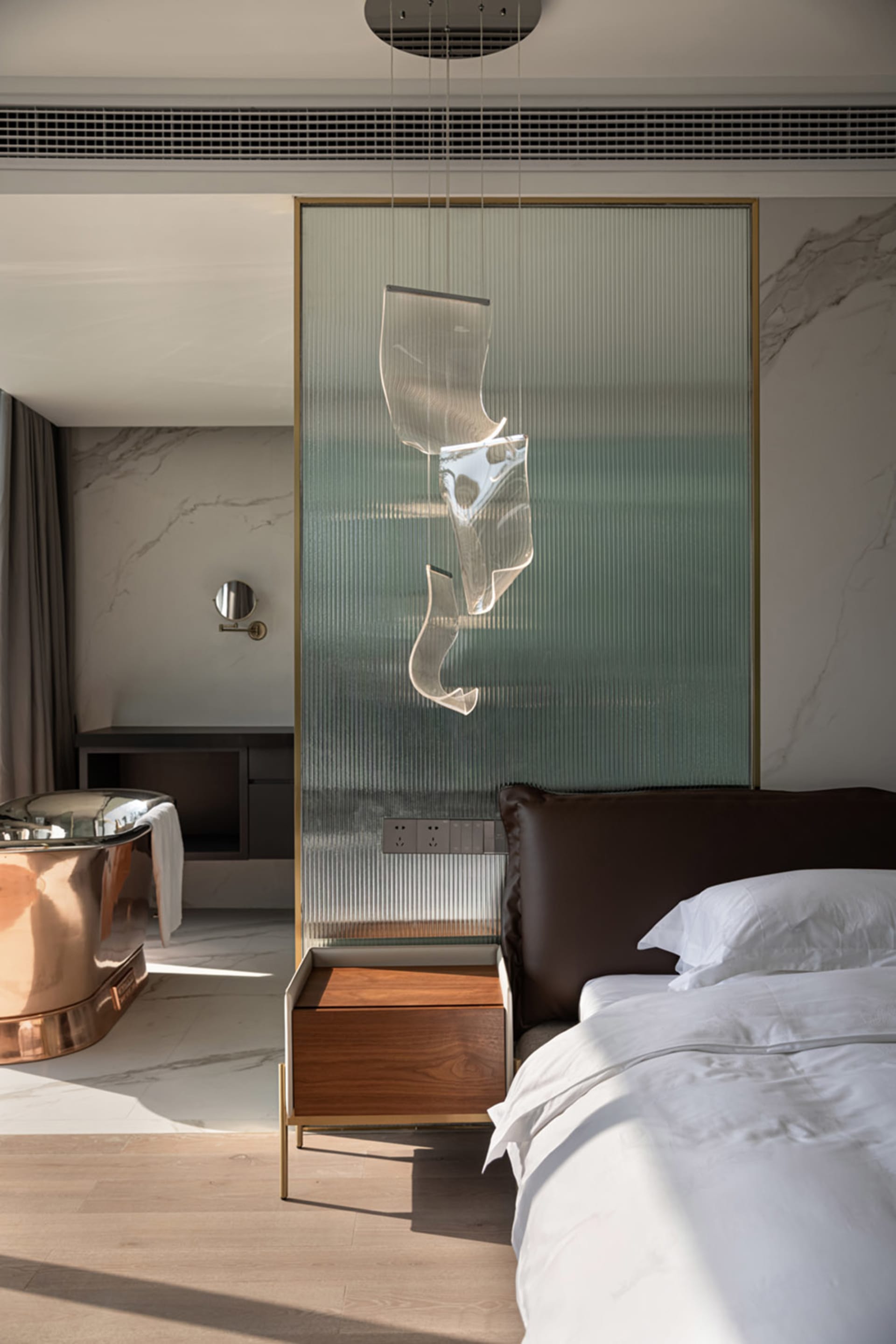 A modern bedroom featuring marble walls, a copper bathtub, leather headboard, and walnut nightstand.