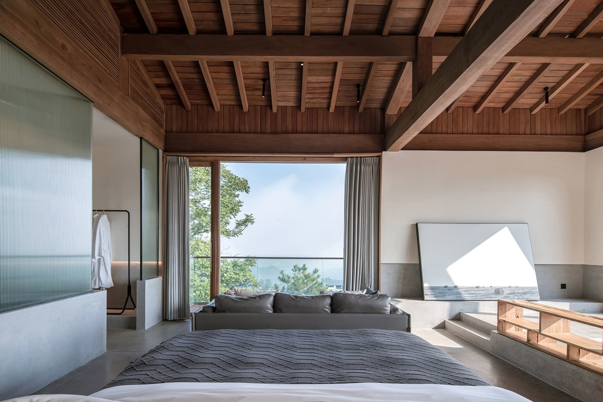 A modern bedroom featuring a bed with a wooden frame and a large window overlooking greenery.