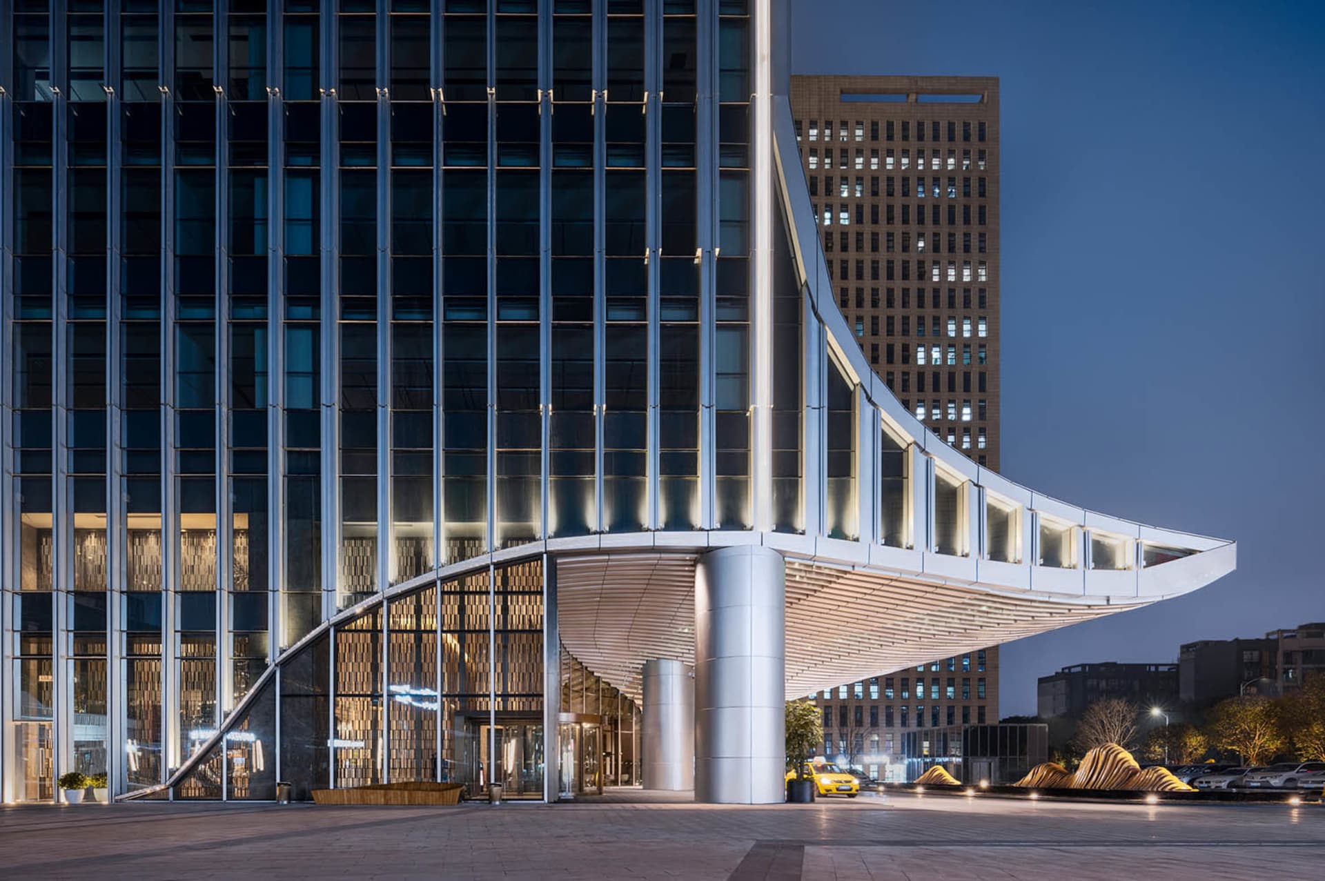 Modern building exterior with glass walls, concrete columns, and an aluminum awning.