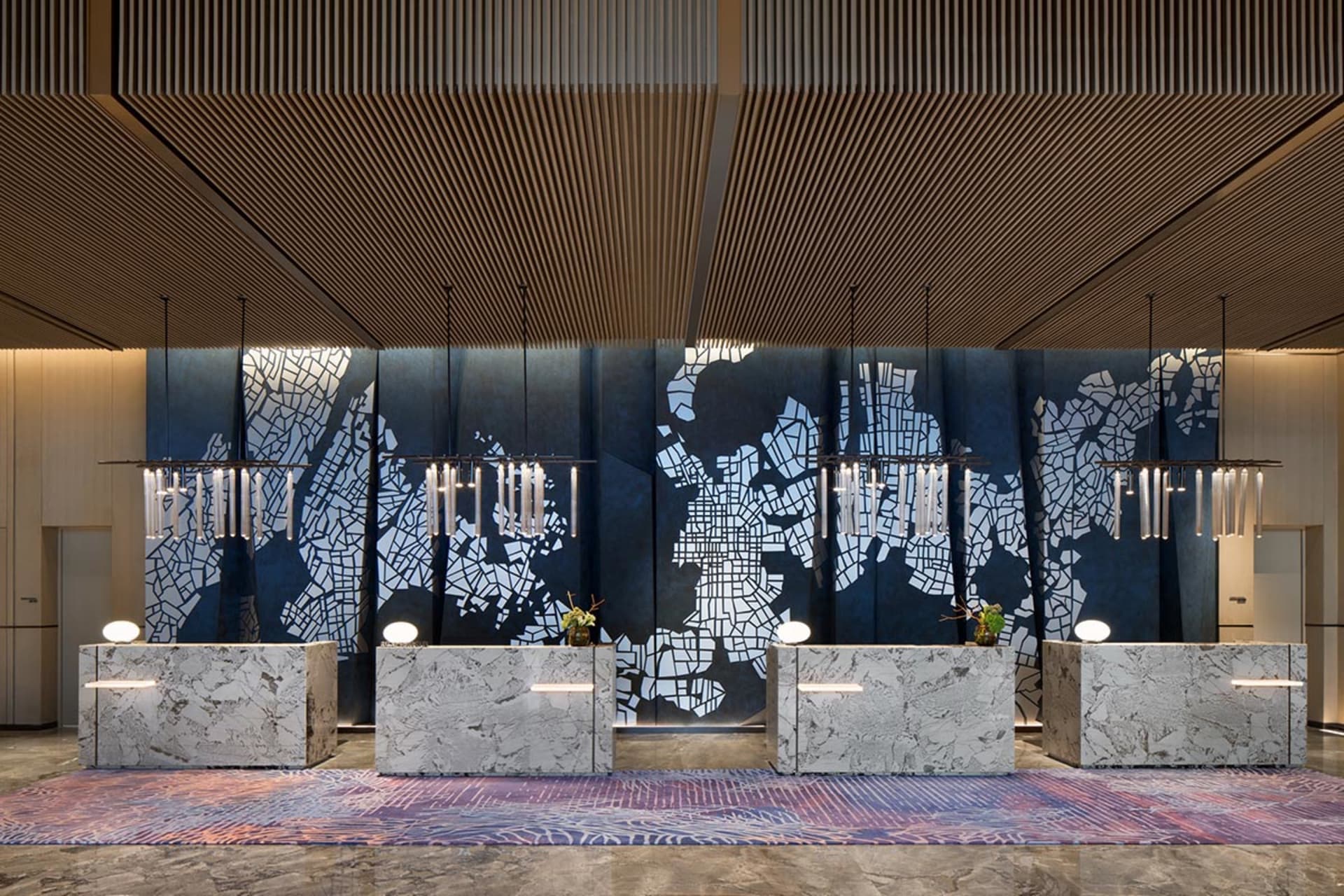 A modern hotel lobby reception area featuring marble countertops, patterned tiles, and illuminated lighting fixtures.
