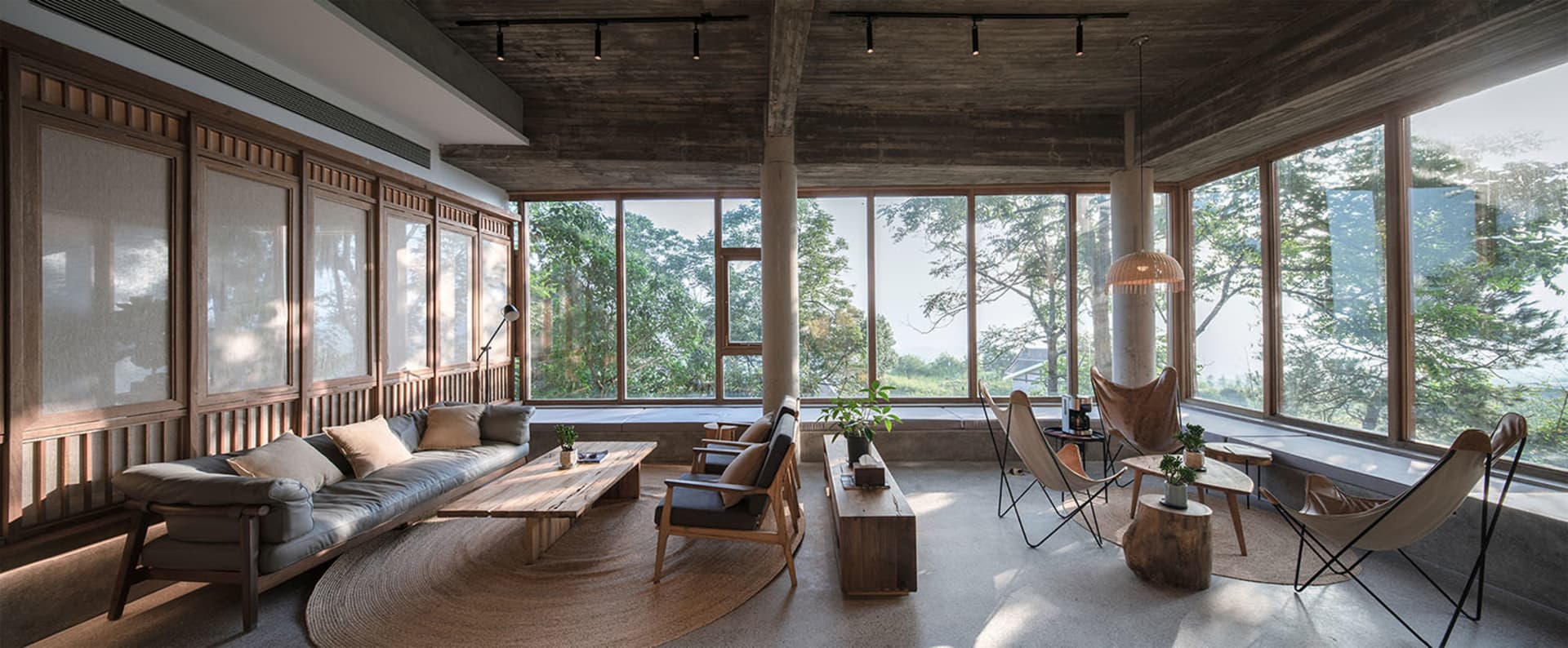 A modern living room featuring concrete walls and floor, with large windows overlooking a scenic outdoor view.