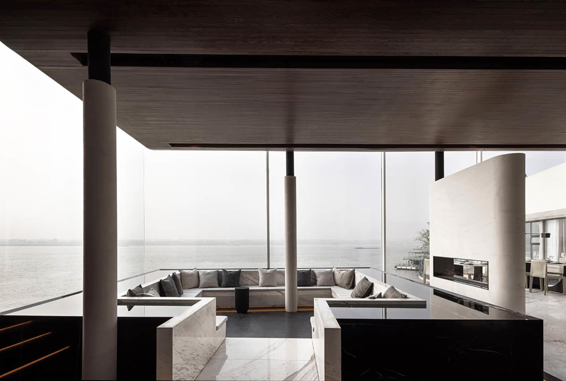 Minimalist living room with marble and concrete materials featuring a large sectional sofa and a panoramic view of the water.