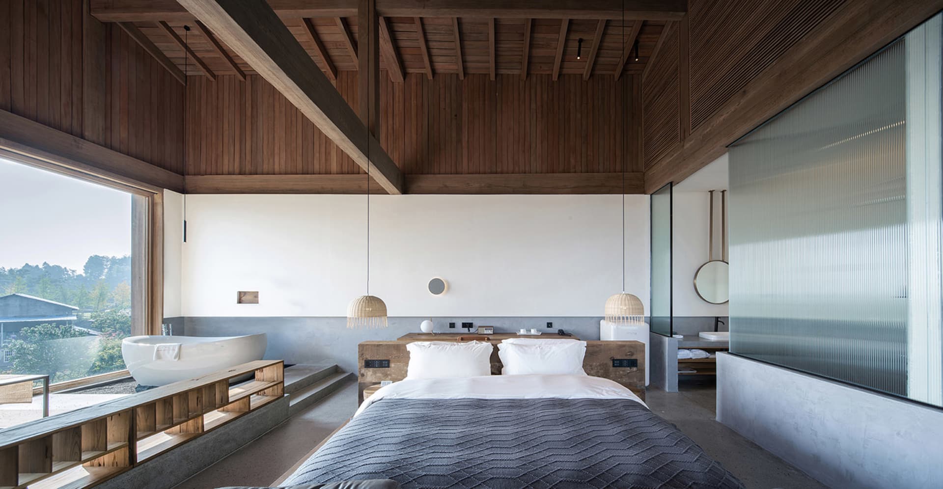 Spacious bedroom with minimalist design, featuring a large bed, wooden floor, and large windows.